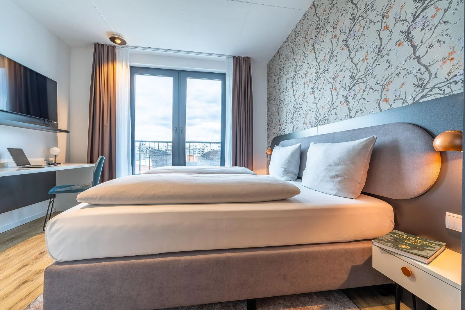 Modernes Doppelzimmer mit Balkonzugang, Schreibtisch und warmem Licht – professionelle Innenaufnahme für Hotelwerbung.