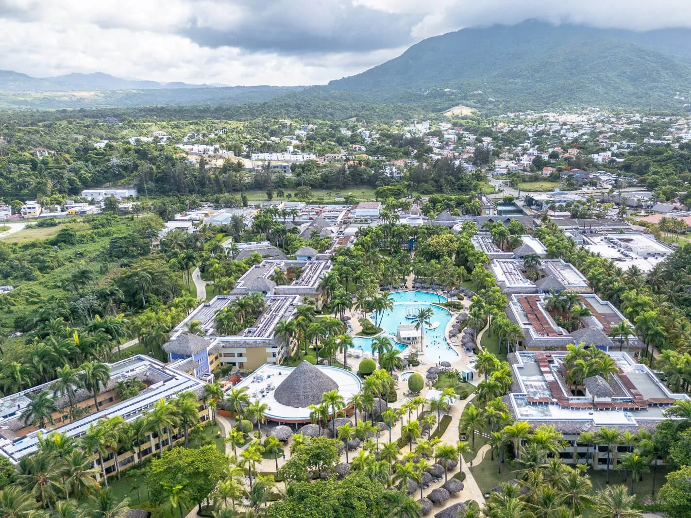 Großflächige Drohnenaufnahme eines Strandresorts mit Palmen, Pool und umliegenden Bergen in Puerto Plata.