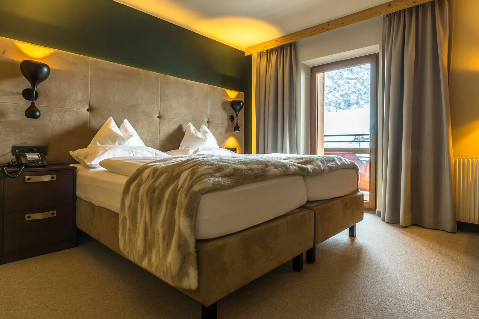 Gemütliches Alpen-Hotelzimmer mit hellen Holzakzenten und Blick auf eine winterliche Berglandschaft.