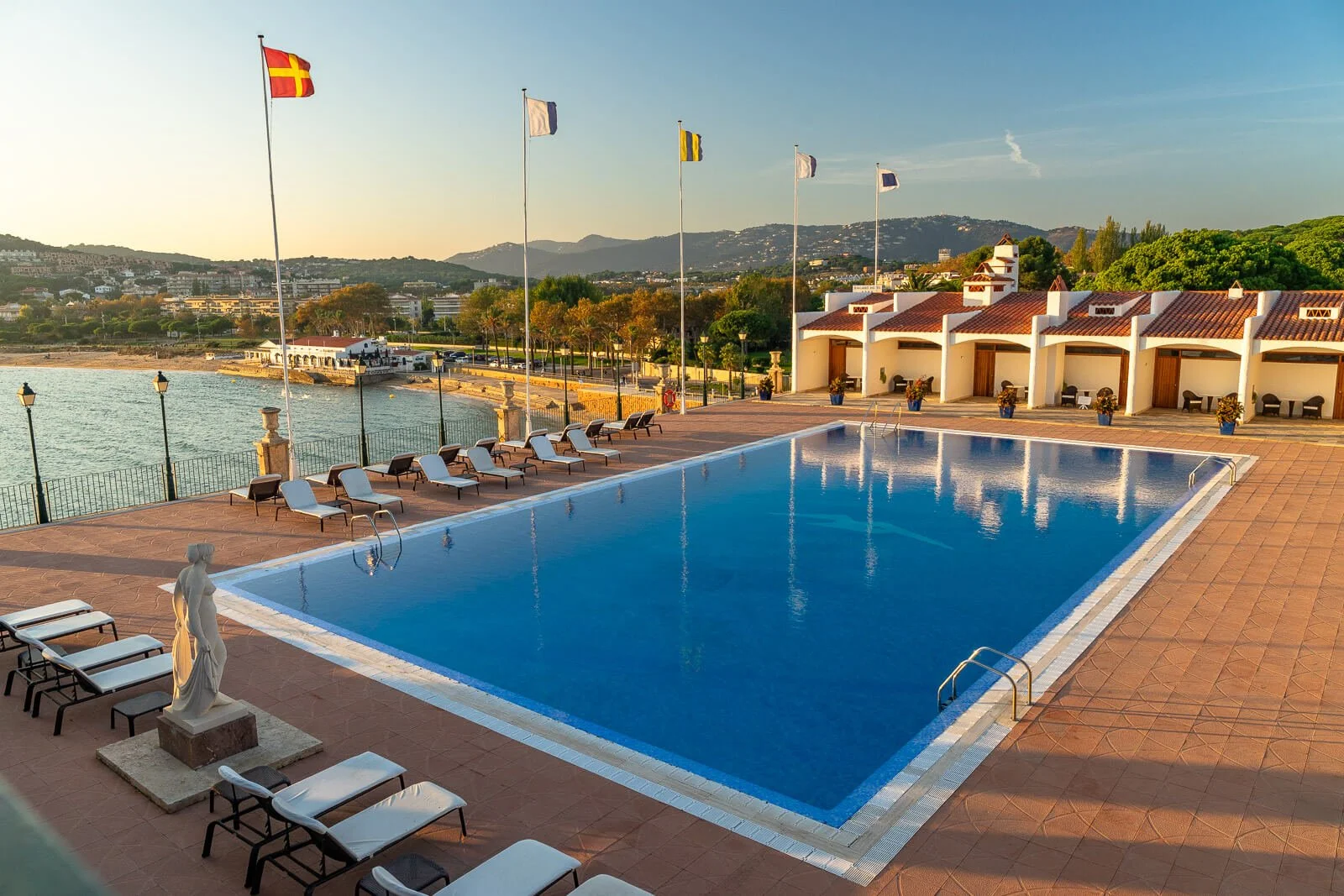 Hotelpool des Hostal de la Gavina an der Costa Brava im goldenen Abendlicht mit Liegen, Flaggen und mediterraner Atmosphäre.