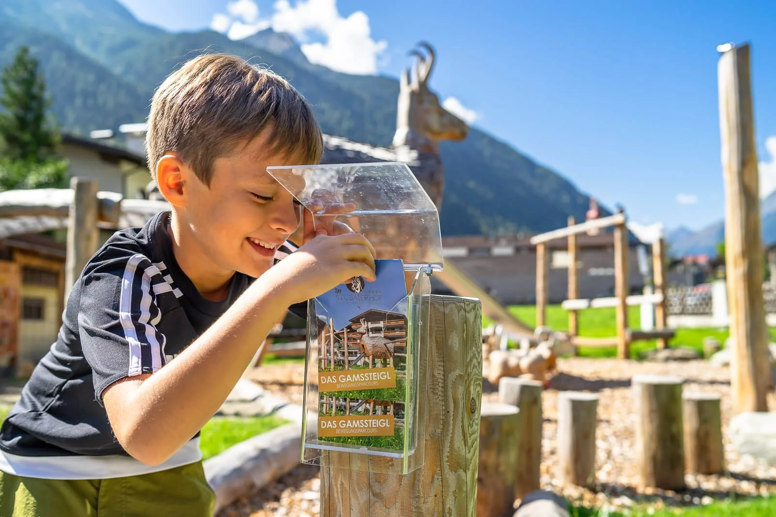 Junge erkundet begeistert den Outdoor-Bewegungsparcours eines Familienhotels in den Alpen bei Sonnenschein.