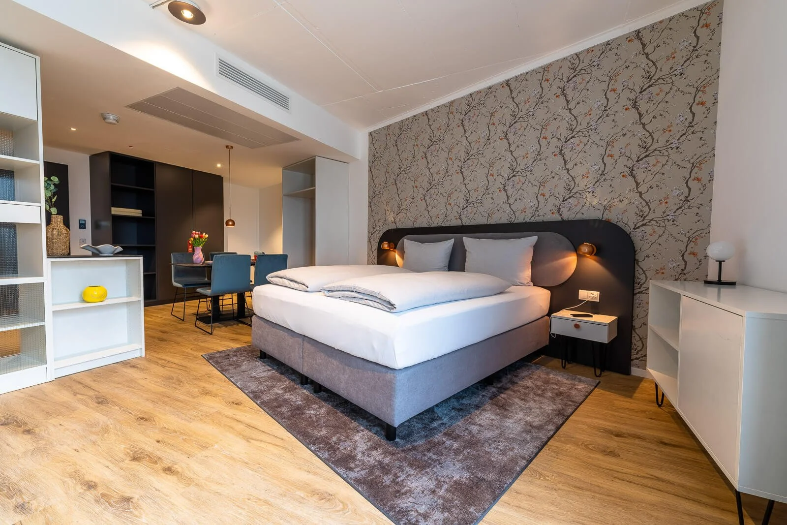 Modernes Hotelzimmer mit großem Doppelbett, Essbereich und heller Holzoptik – professionelles Interior-Foto für Hotelmarketing.