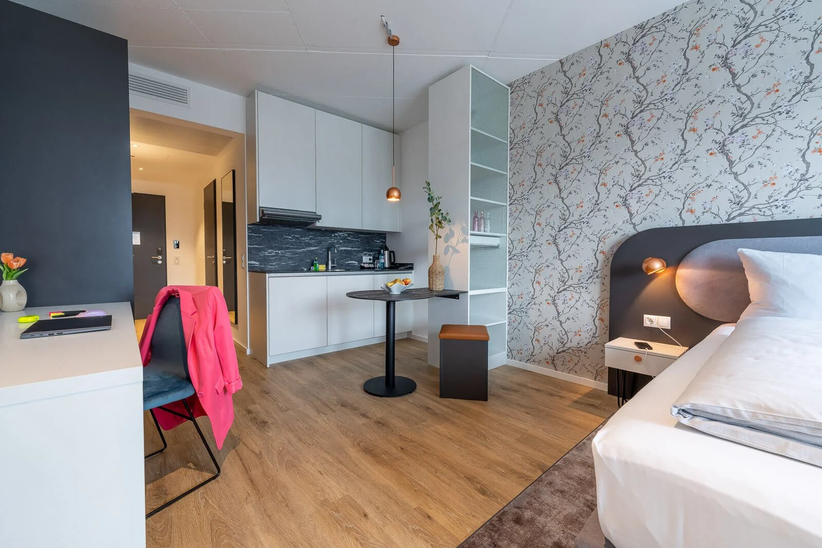 Modernes Hotelstudio mit Küchenzeile, Esstisch und grafischer Tapete – professionelle Interiorfotografie.