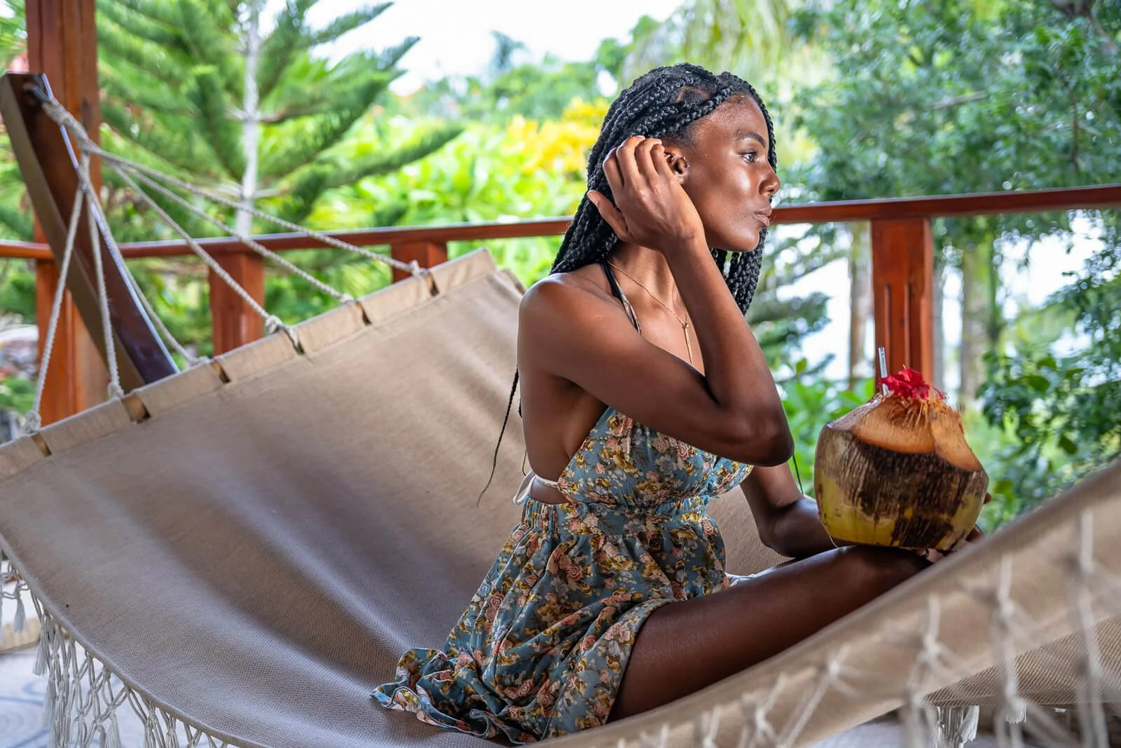 Gast relaxt in einer Hängematte mit frischer Kokosnuss, umgeben von tropischer Vegetation und Holzveranda.