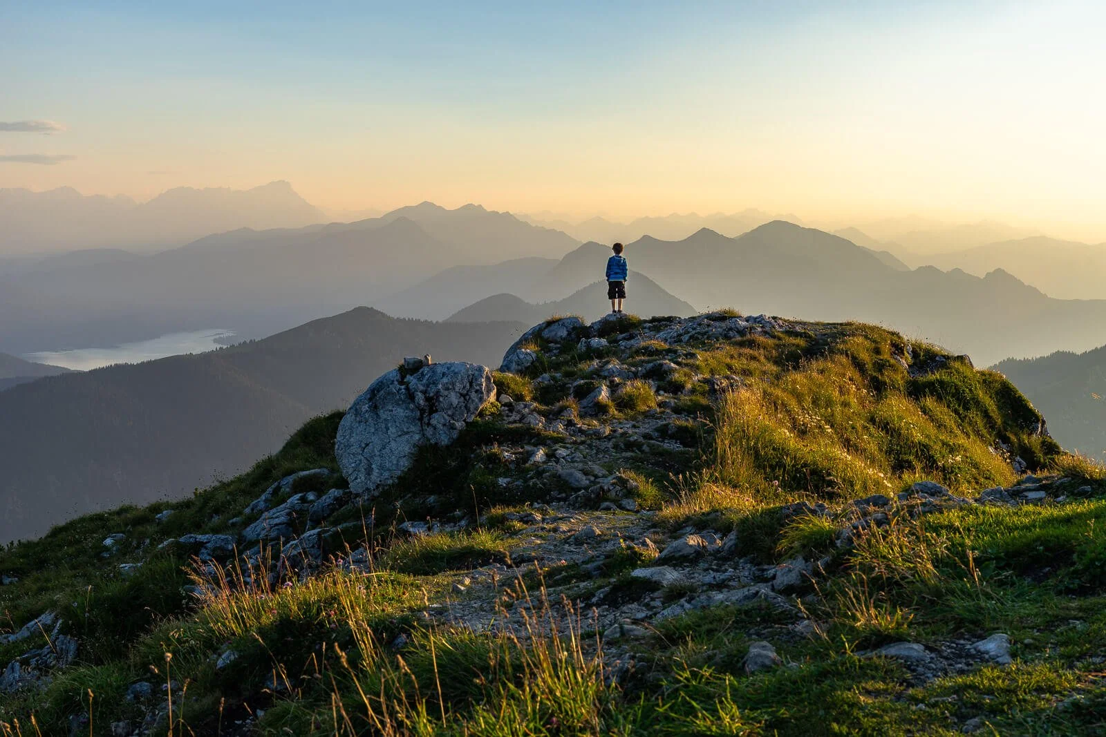 Junge steht bei Sonnenuntergang auf der Benediktenwand und blickt über die Bayerischen Alpen