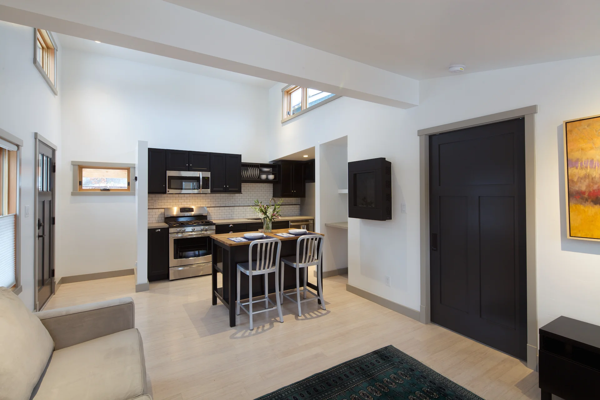 The small window by the front door has a sweet view of distant hills and is the only west-facing window in the cottage, to prevent overheating. High windows and a ceiling fan will ventilate the space in the summer time. In this photo, the pocket door to the bedroom is closed. 