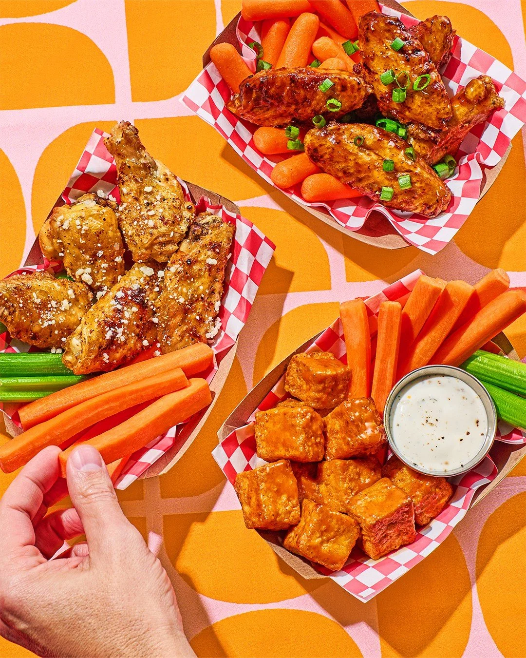 Commercial photography of a hand coming in and three plates of wings