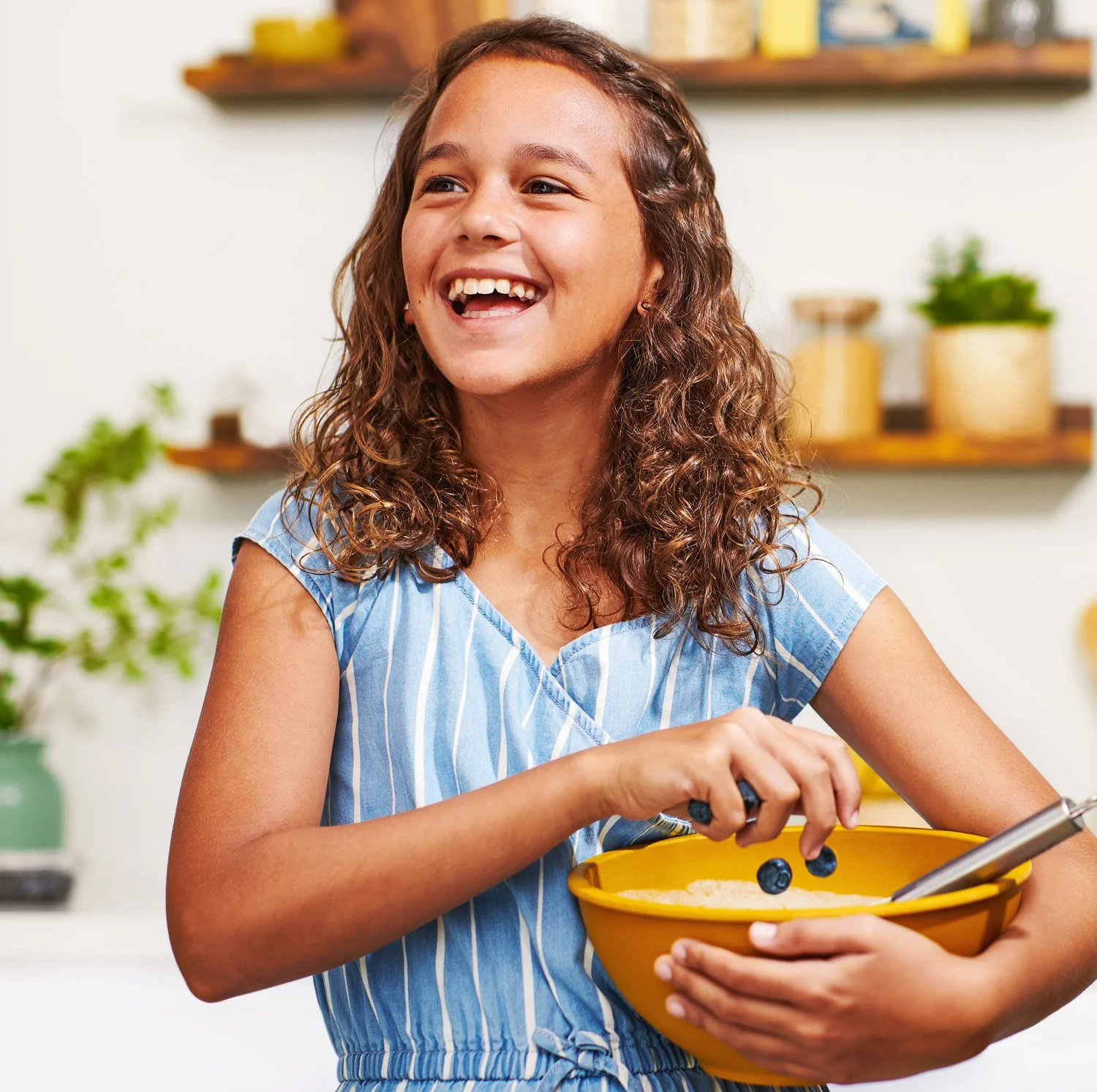 Commercial photography of a girl holding a bowl of pancake batter and dropping in blueberries