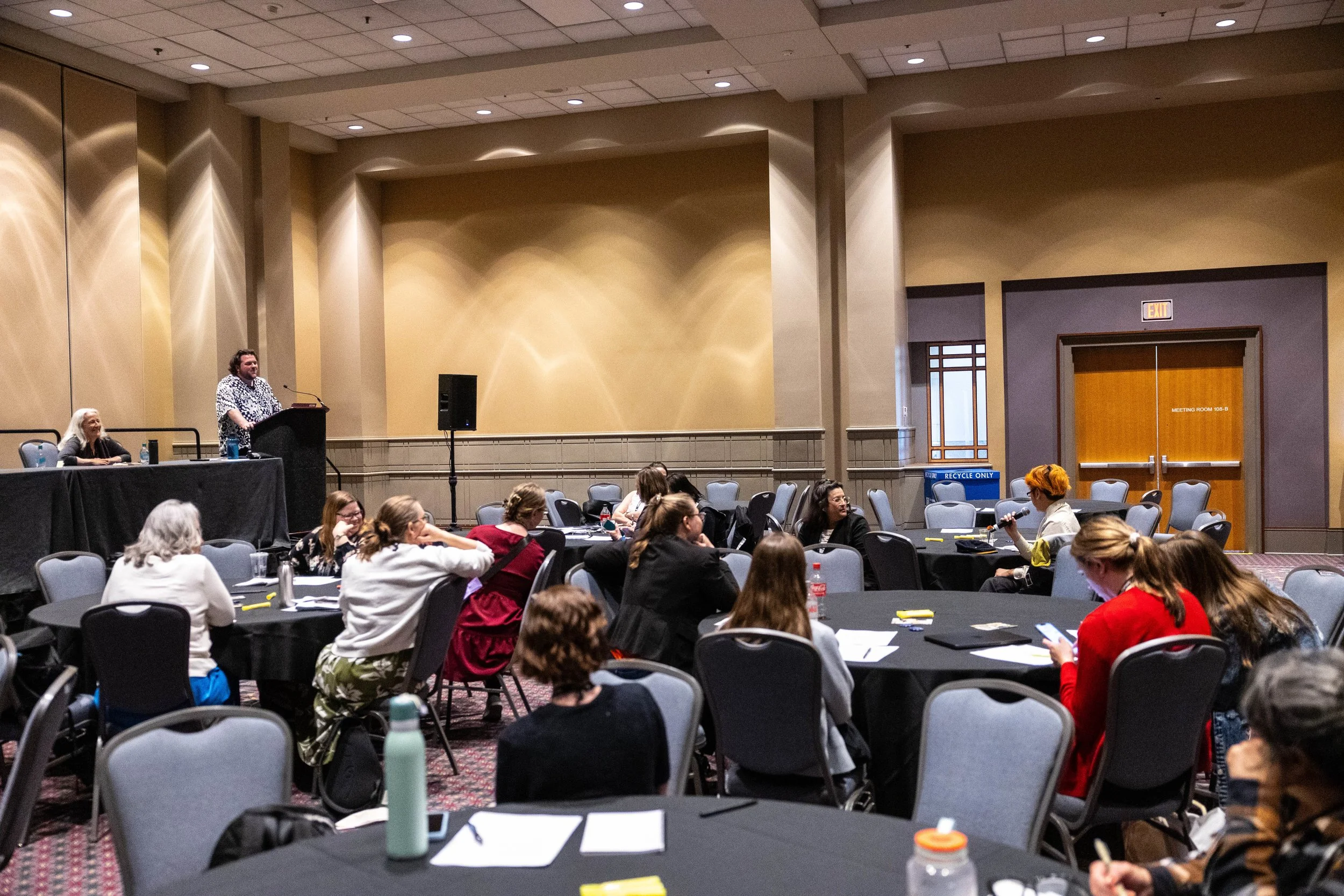 The 2026 AAM Conference, with B.O’Mahoney and E.Rifkin leading a discussion with a group of roughly a dozen pictured individuals, one of which holds a mic to ask a question.