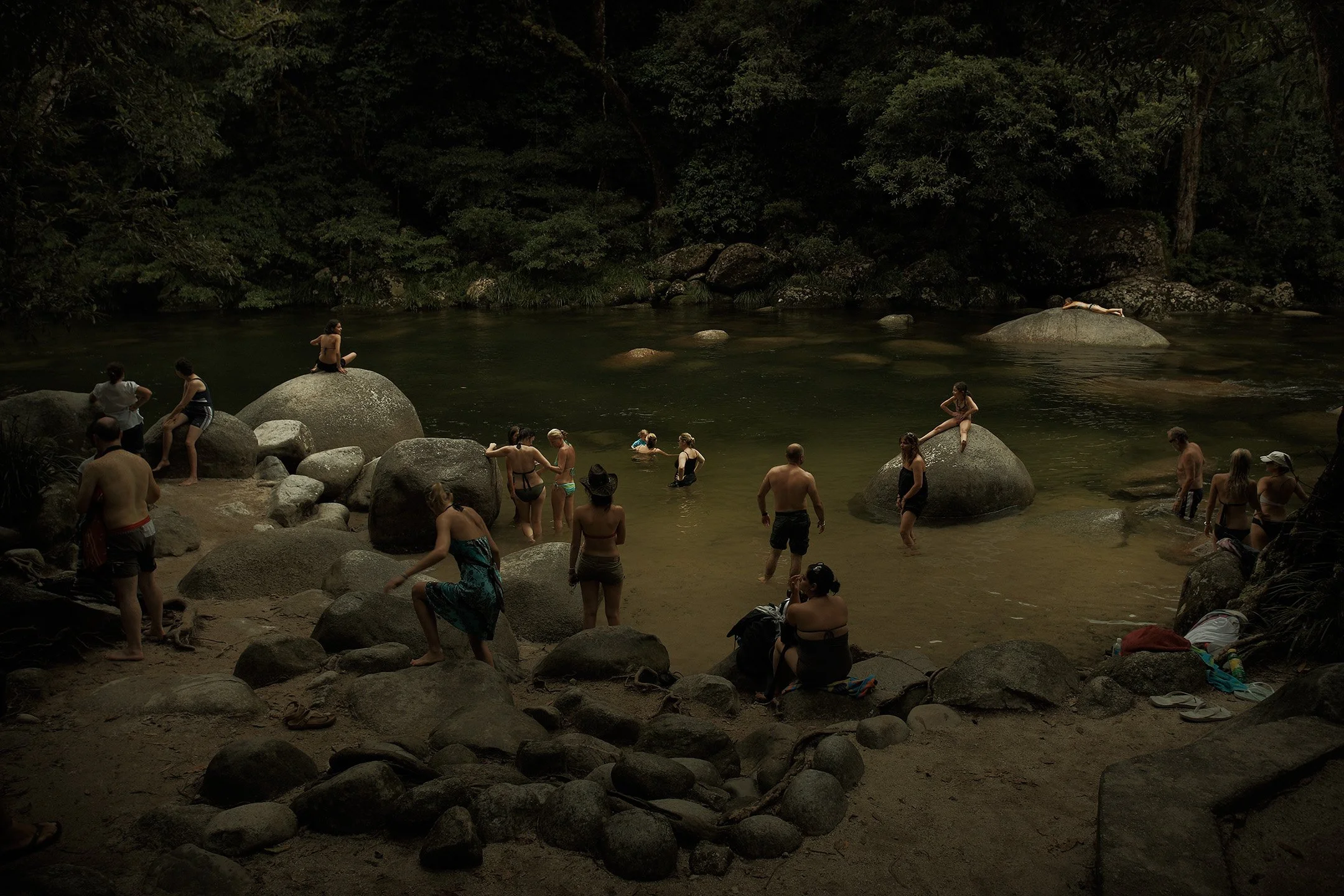 People swimming and relaxing in a river surrounded by large rocks and dense trees.