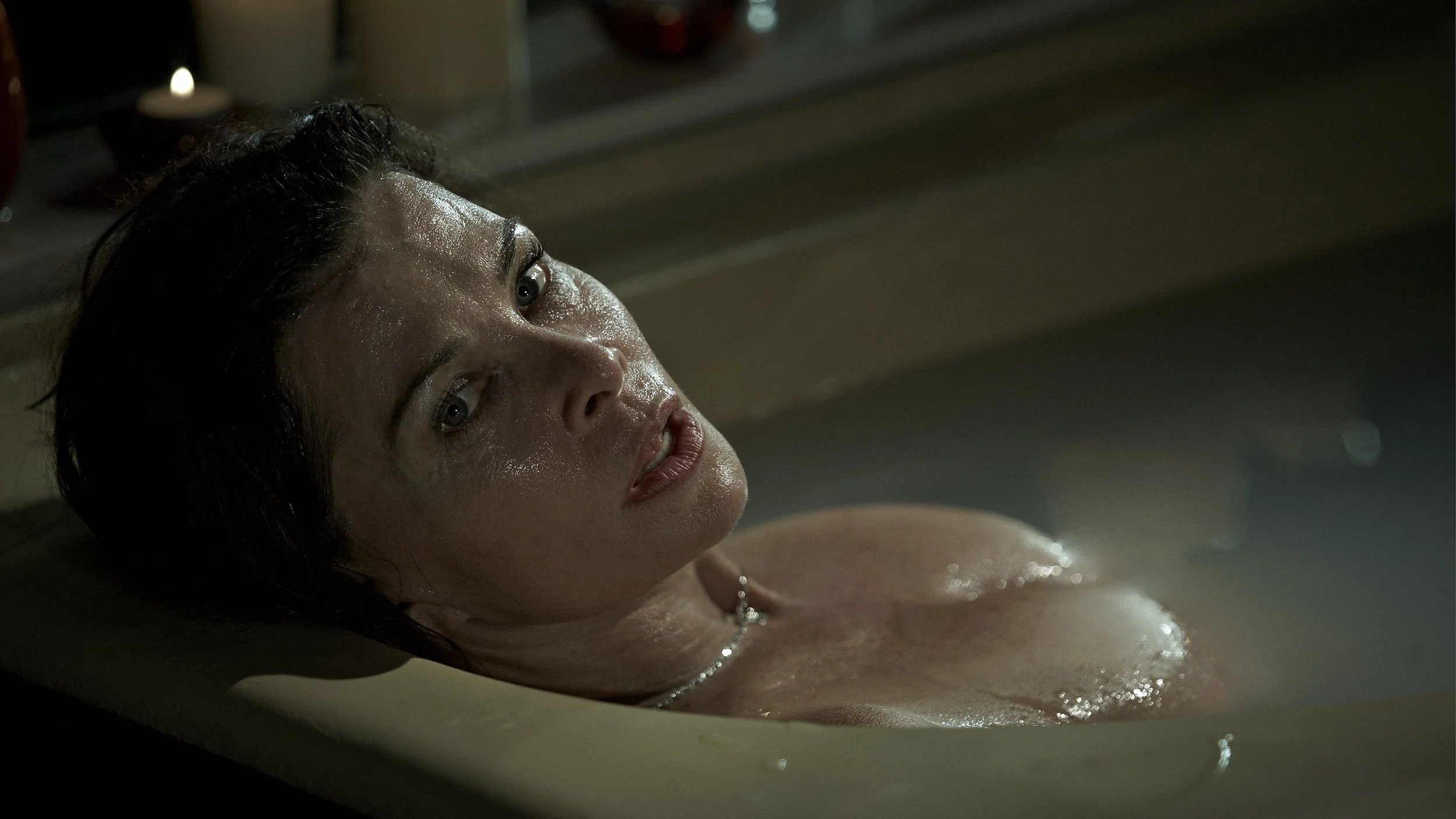 A woman with dark hair and makeup lying partially submerged in water, looking up.