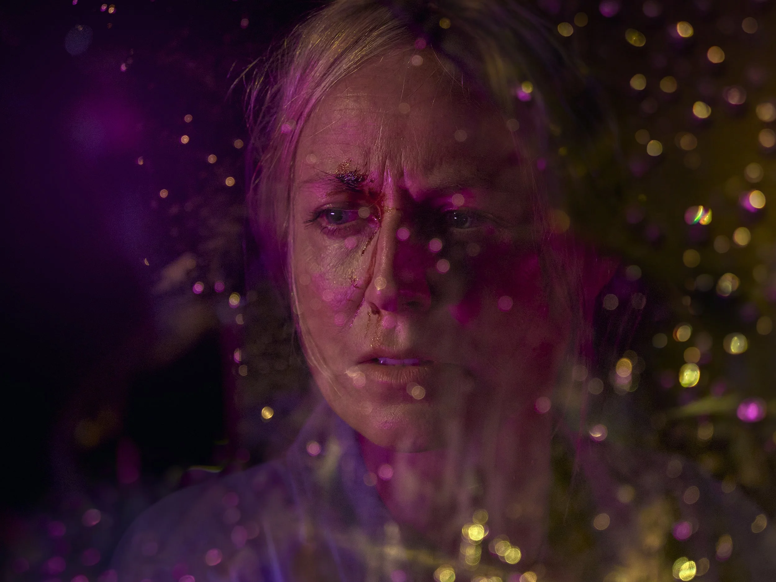 A close-up of a woman's face surrounded by multicolored bokeh lights, with a focus on her closed eyes and serene expression.
