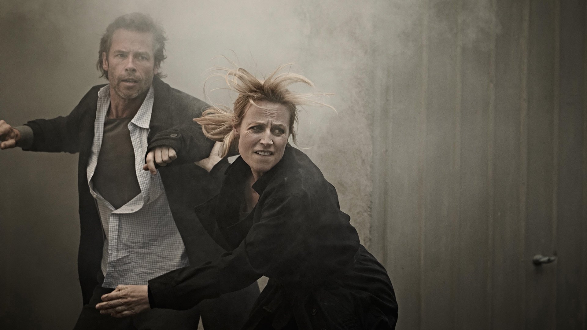 A man and woman are engaged in a physical altercation, with the man grabbing the woman's arm and the woman looking distressed as she leans against a wall. Featuring Guy Pearce & Marta Dusseldorp