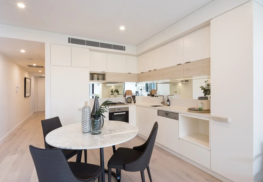 Modern white kitchen with wooden accents, a marble dining table, and black chairs.