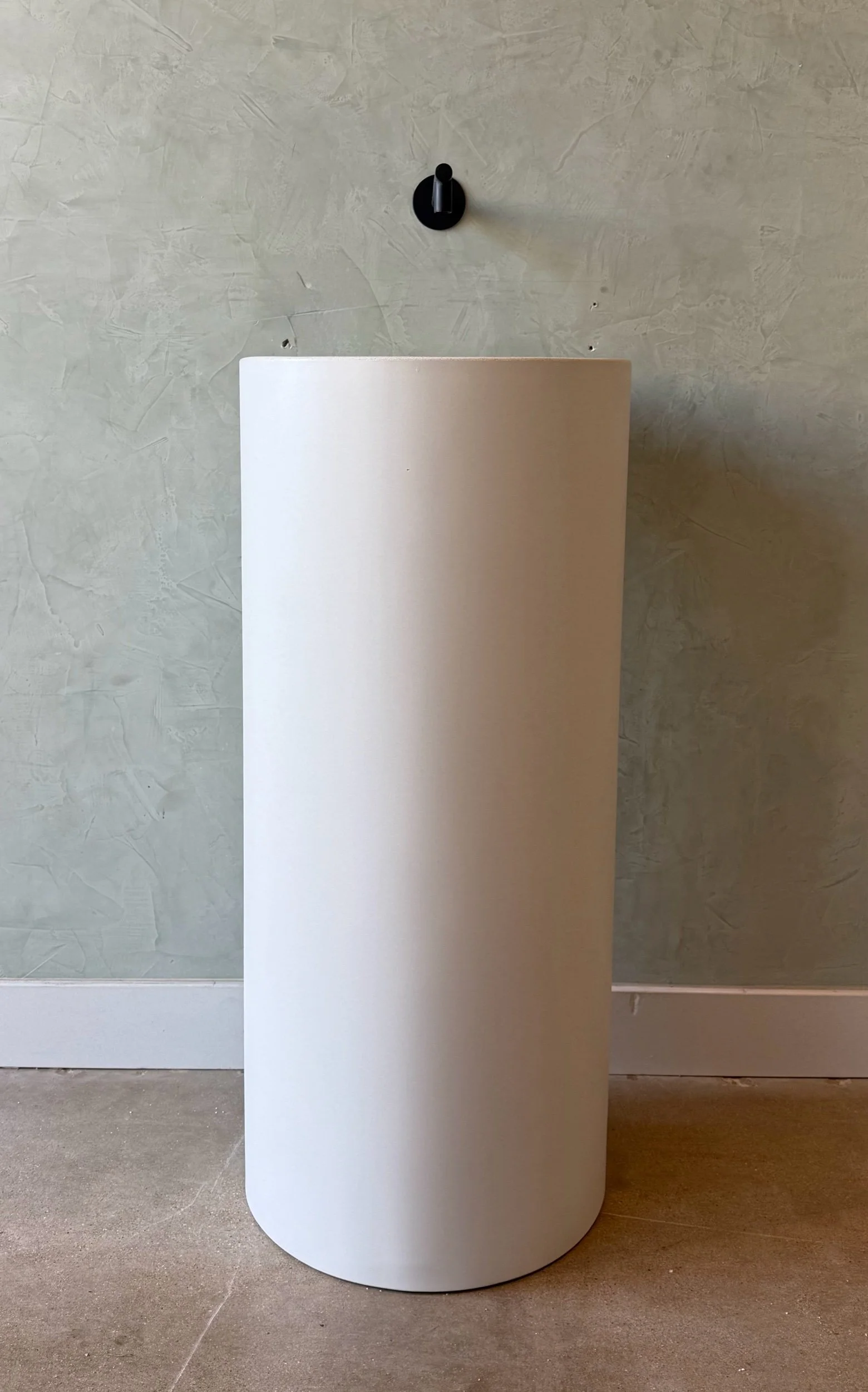 Front view of a white freestanding concrete pedestal sink, showcasing its sculptural round form and modern aesthetic