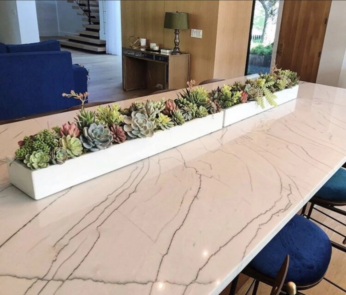 Two white 36-inch concrete planters installed as a long centerpiece on an oversized marble dining table, filled with succulents