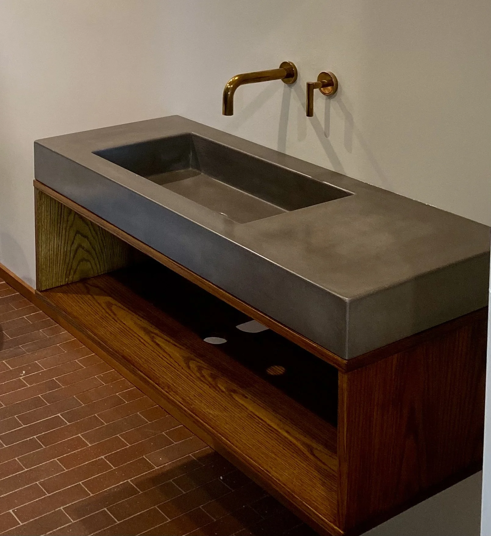 Medium grey farmhouse concrete sink on dark wood vanity, side view, wall-mounted faucet