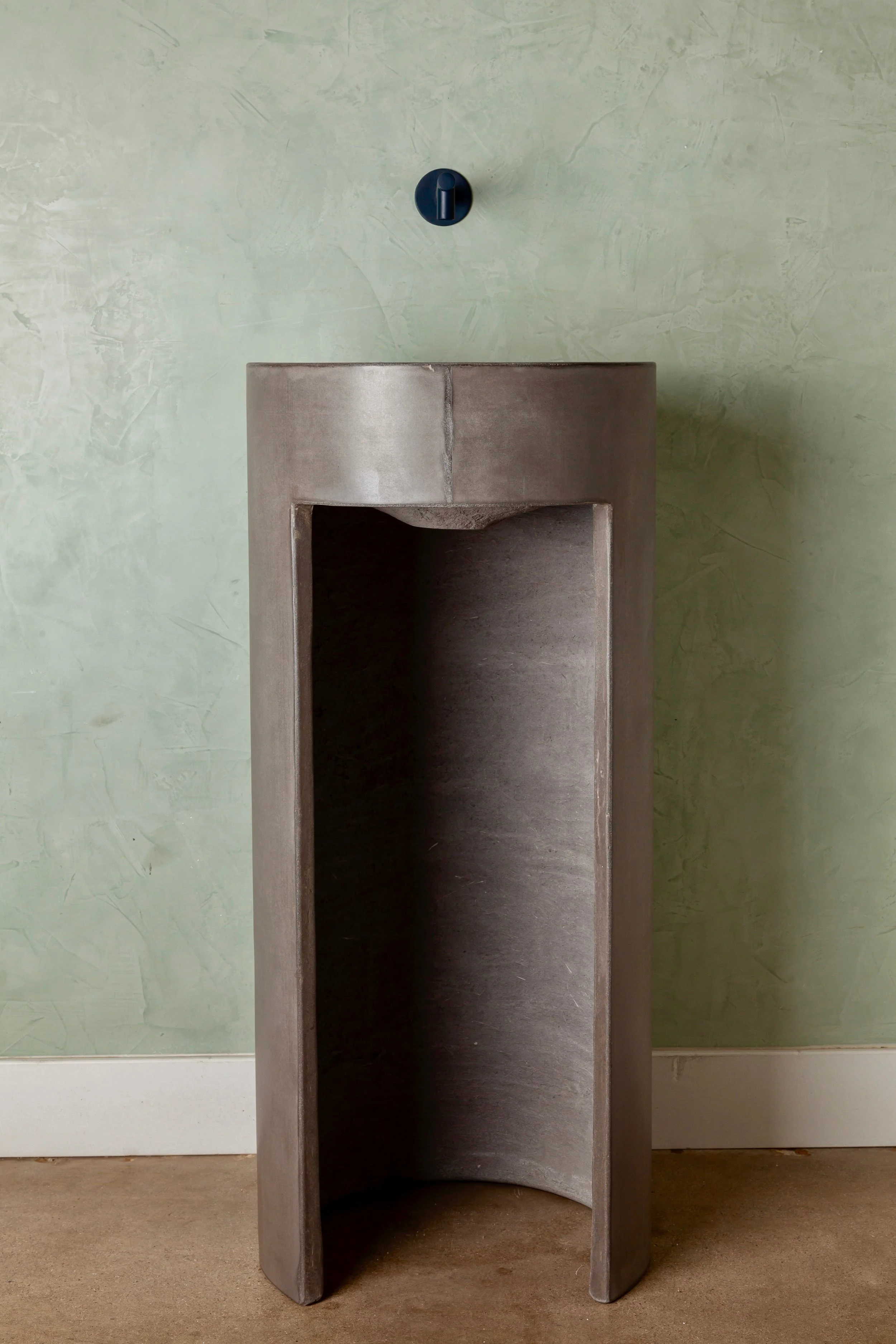 Rear view of dark grey freestanding concrete pedestal sink showing rear plumbing access opening