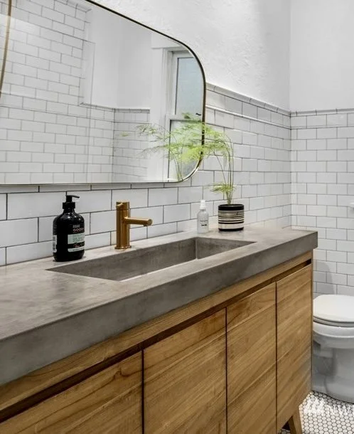 Medium grey farmhouse concrete sink on light wood vanity with bronze faucet, full white tile bathroom