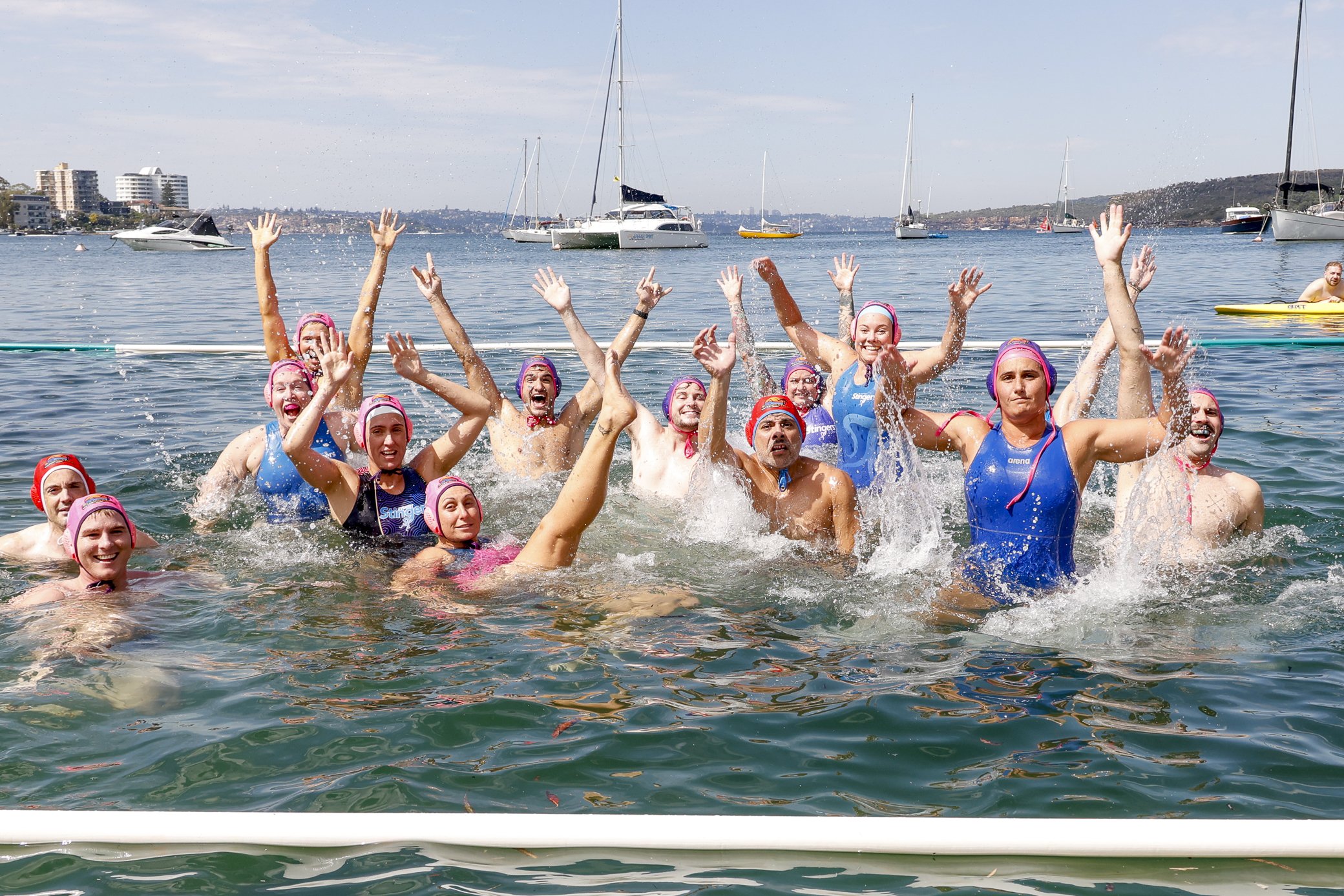 Sydney Stingers members standing waist-deep in open water with arms raised, smiling and celebrating together.