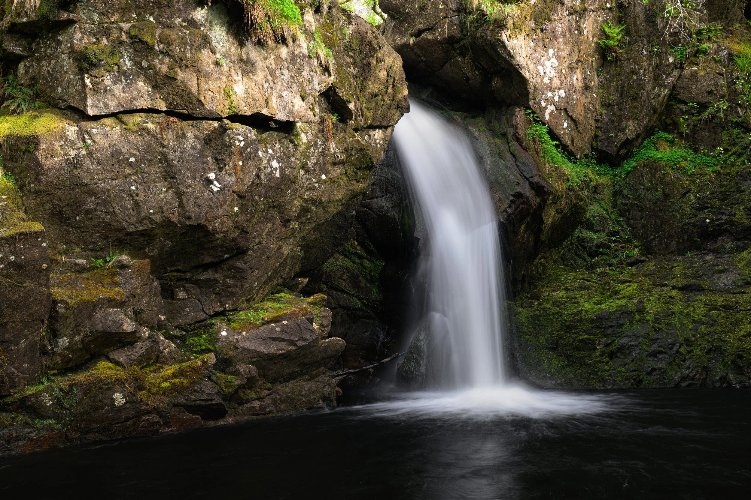 A photograph of a waterfall deep in the Scottish highlands.