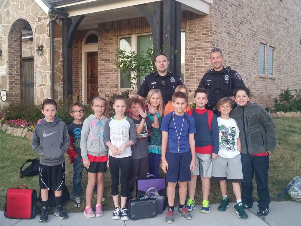 Officer Kyle Schwanz and Officer Doug Williams at the bus stop with Harvest kiddos