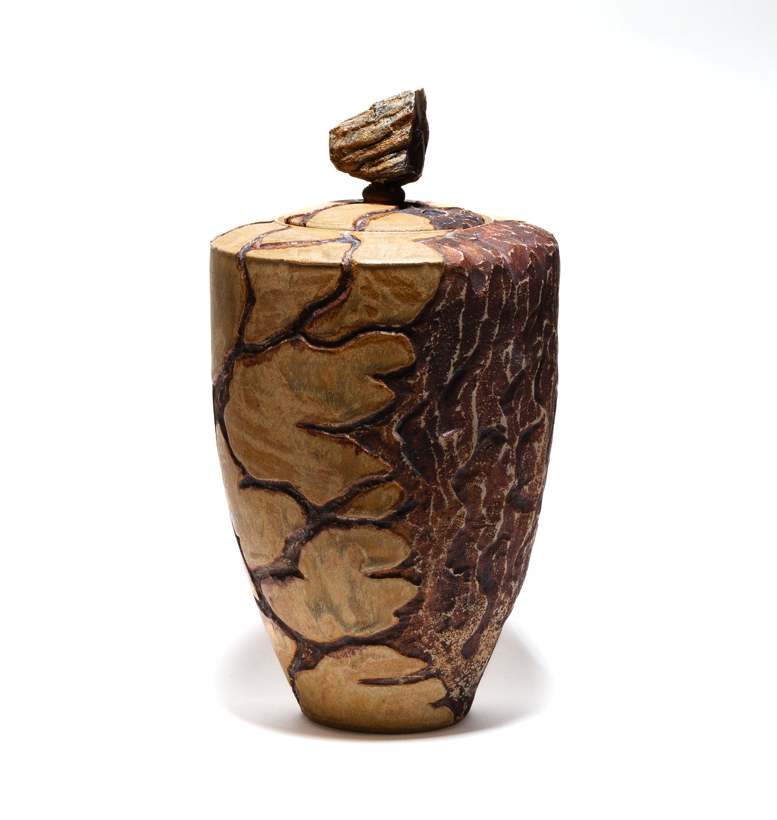 A ceramic sculpture of a human head with a landscape and forest pattern, topped with a small rock balanced on top.