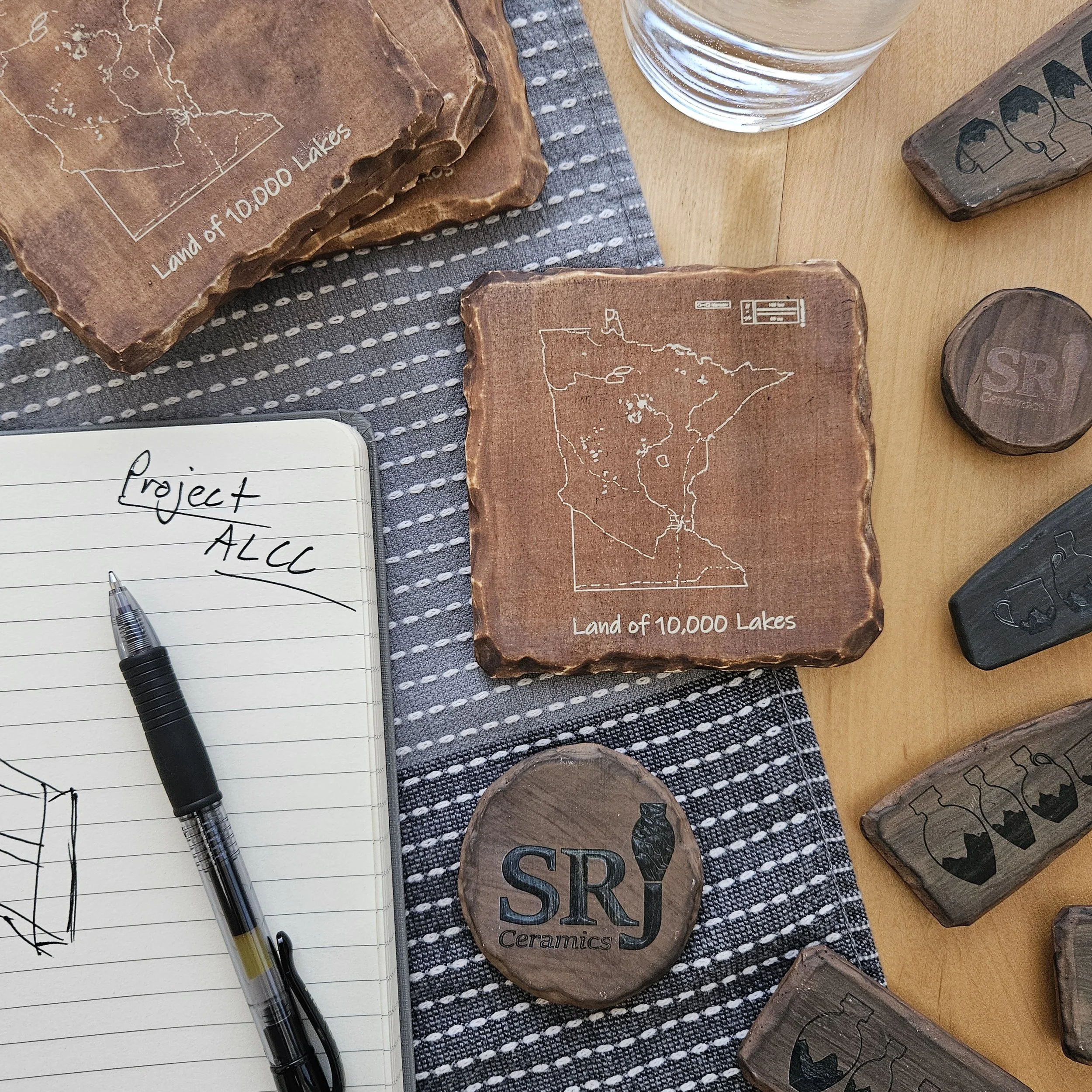 Several carved stone blocks with outlines and labels, a glass of water, a pen, a notepad, and small carved wooden blocks on a wooden table.