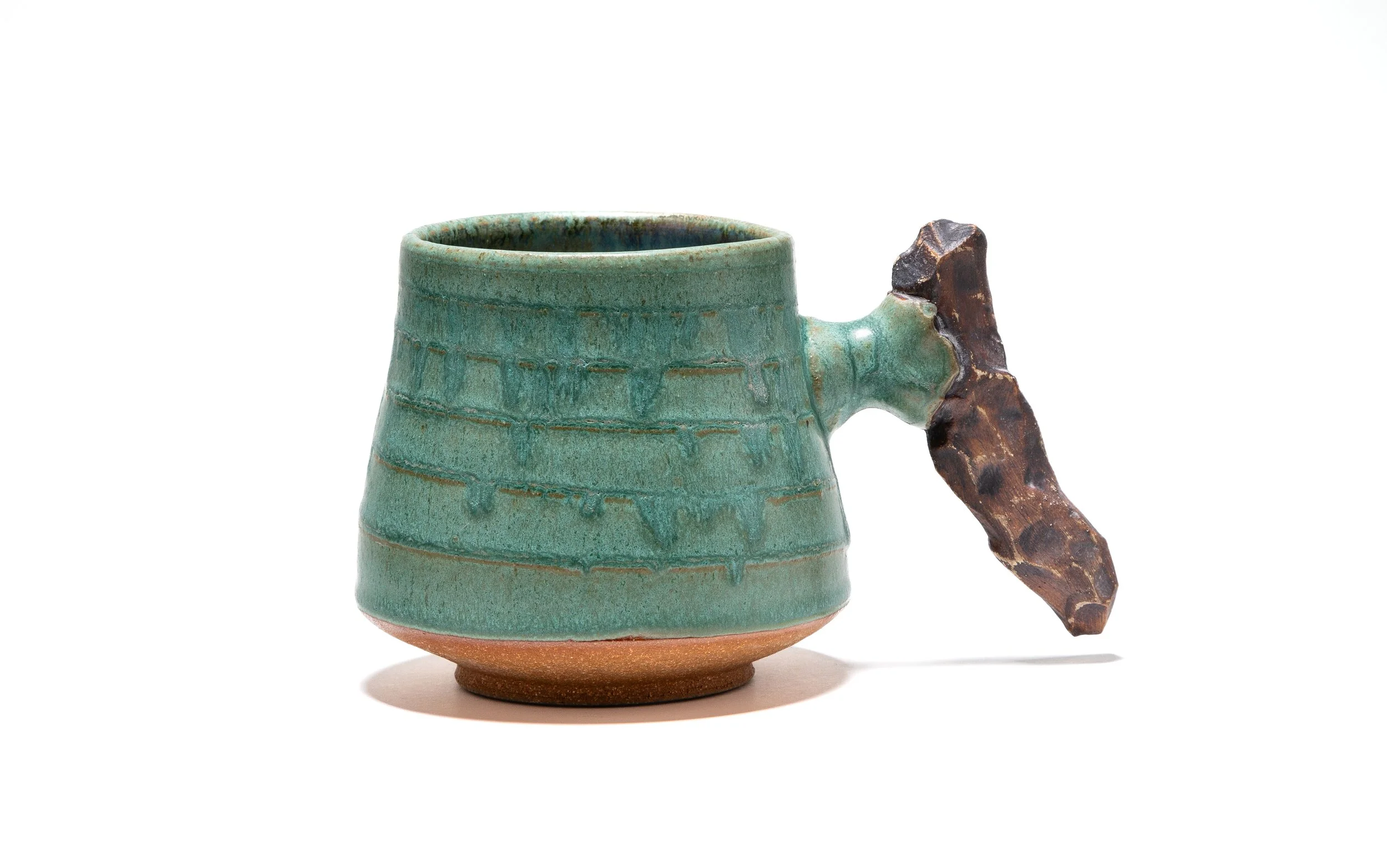 A ceramic mug with a green glazed surface and a textured, dark brown, branch-like handle against a white background.
