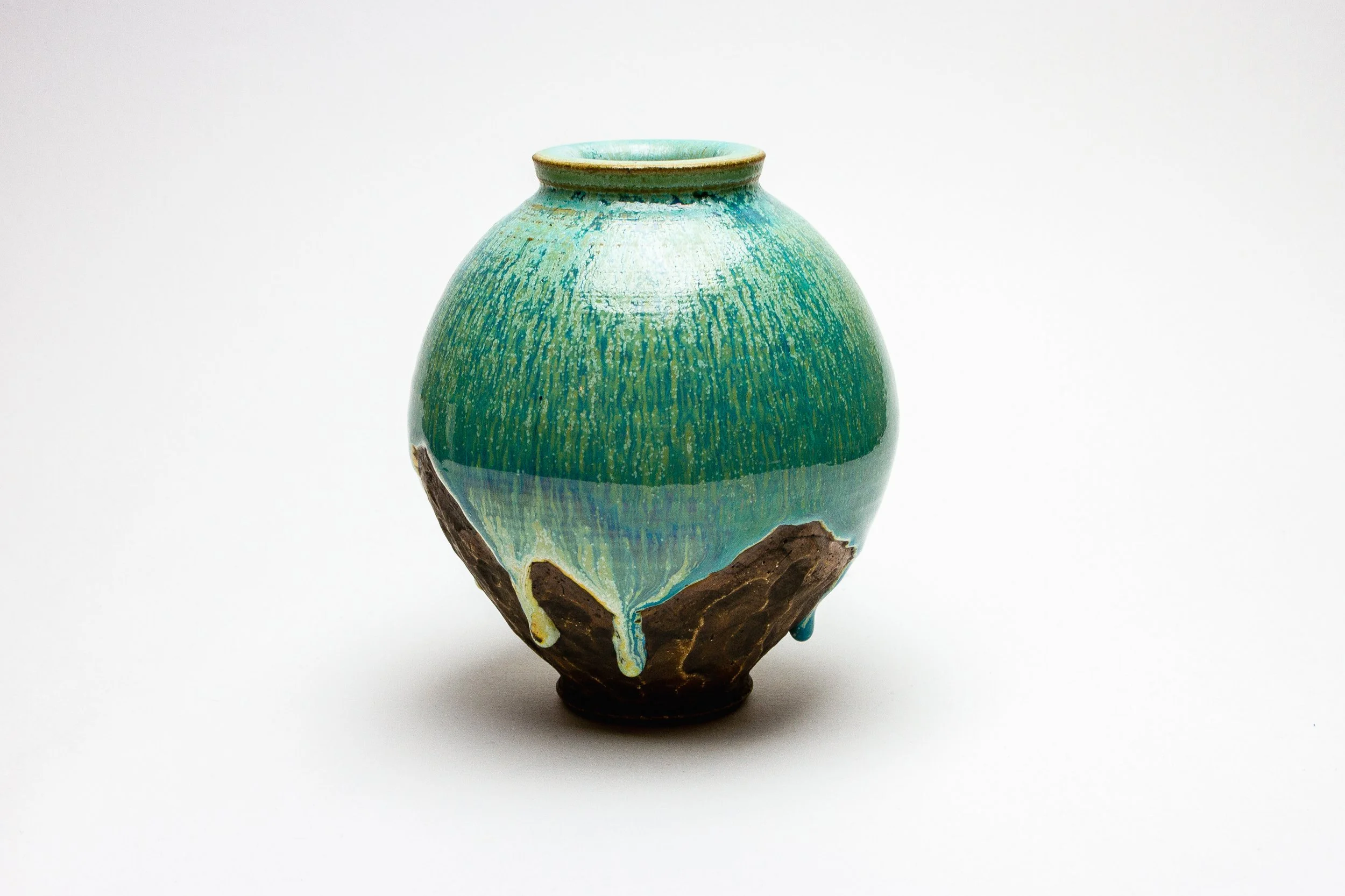 A ceramic vase with a rounded body and narrow neck, decorated with green, blue, and earthy tones, showing signs of weathering and a partially broken base.