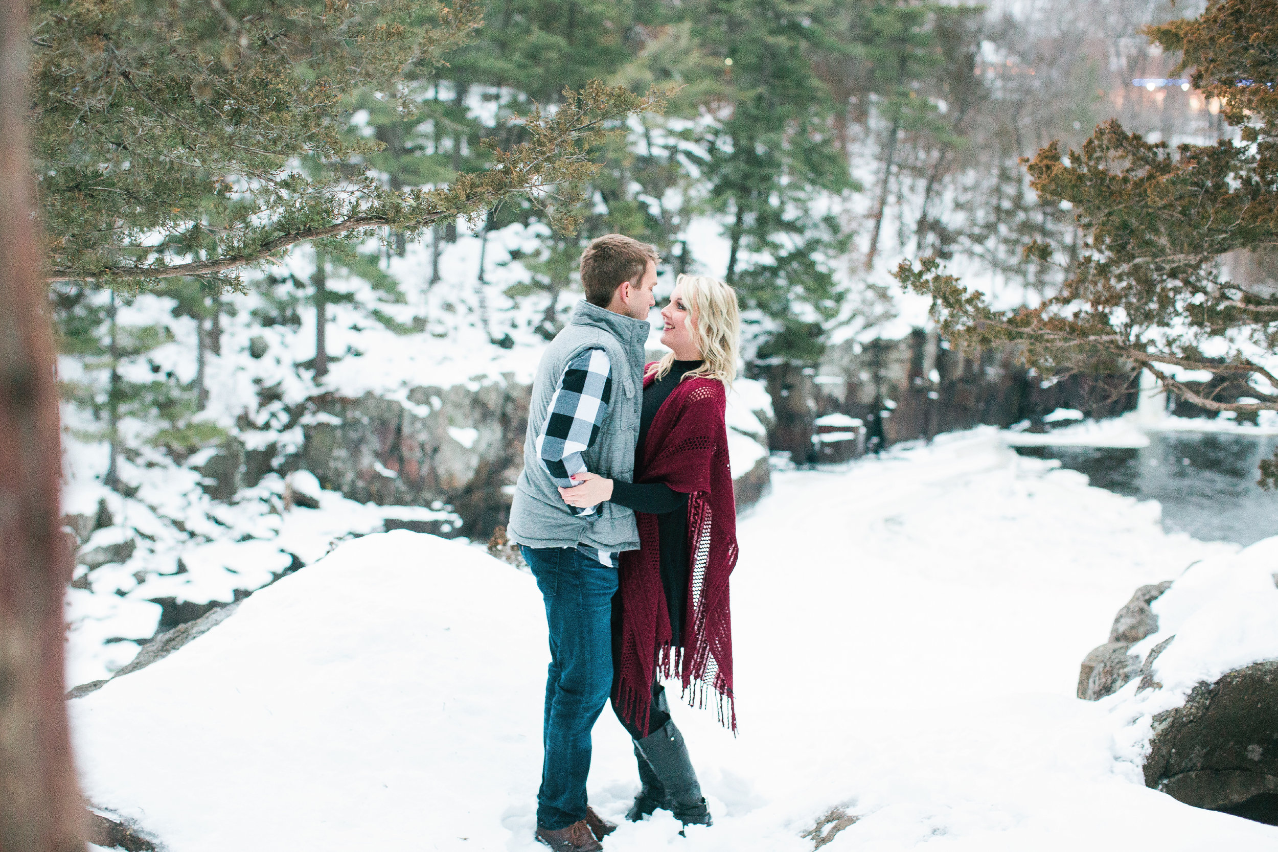 Snowy Minnesota Taylors Falls winter engagement photos on bluff overlooking river and woods in burgundy shawl, plaid vest