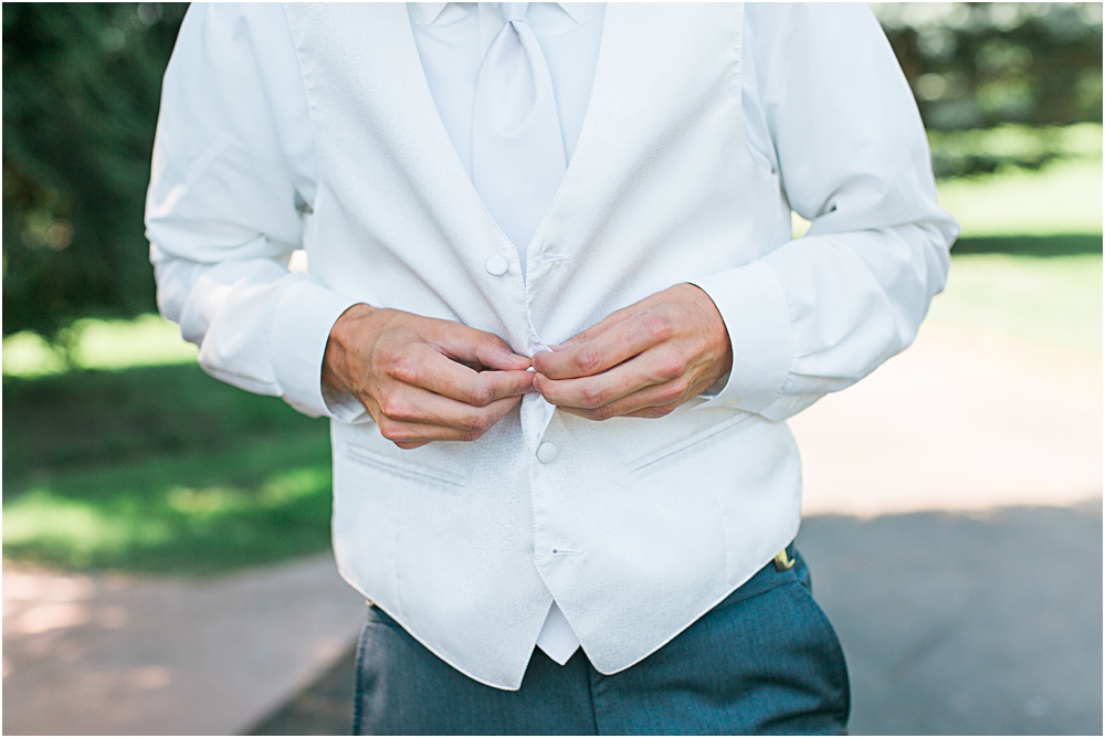 Groom getting ready for Minnesota summer wedding day in white vest