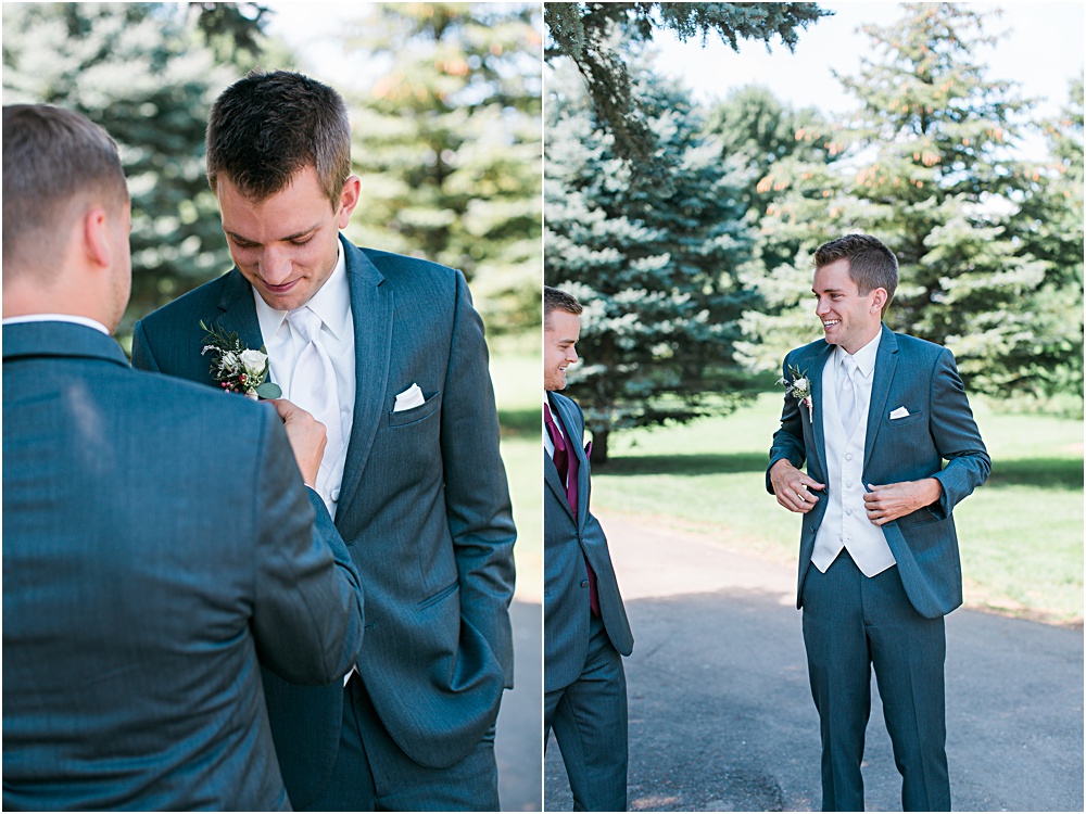 Groom getting ready for Minnesota summer wedding day in dark gray suit and white vest best man helping groom into suit