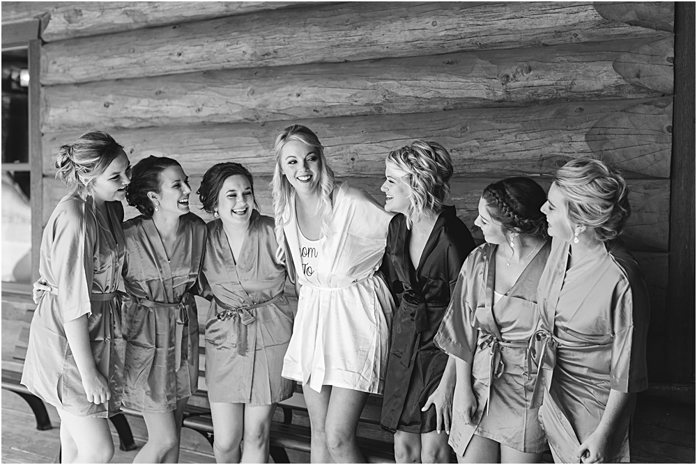 Minnesota summer wedding bride and bridesmaids laughing in coordinating robes in front of cabin in black and white
