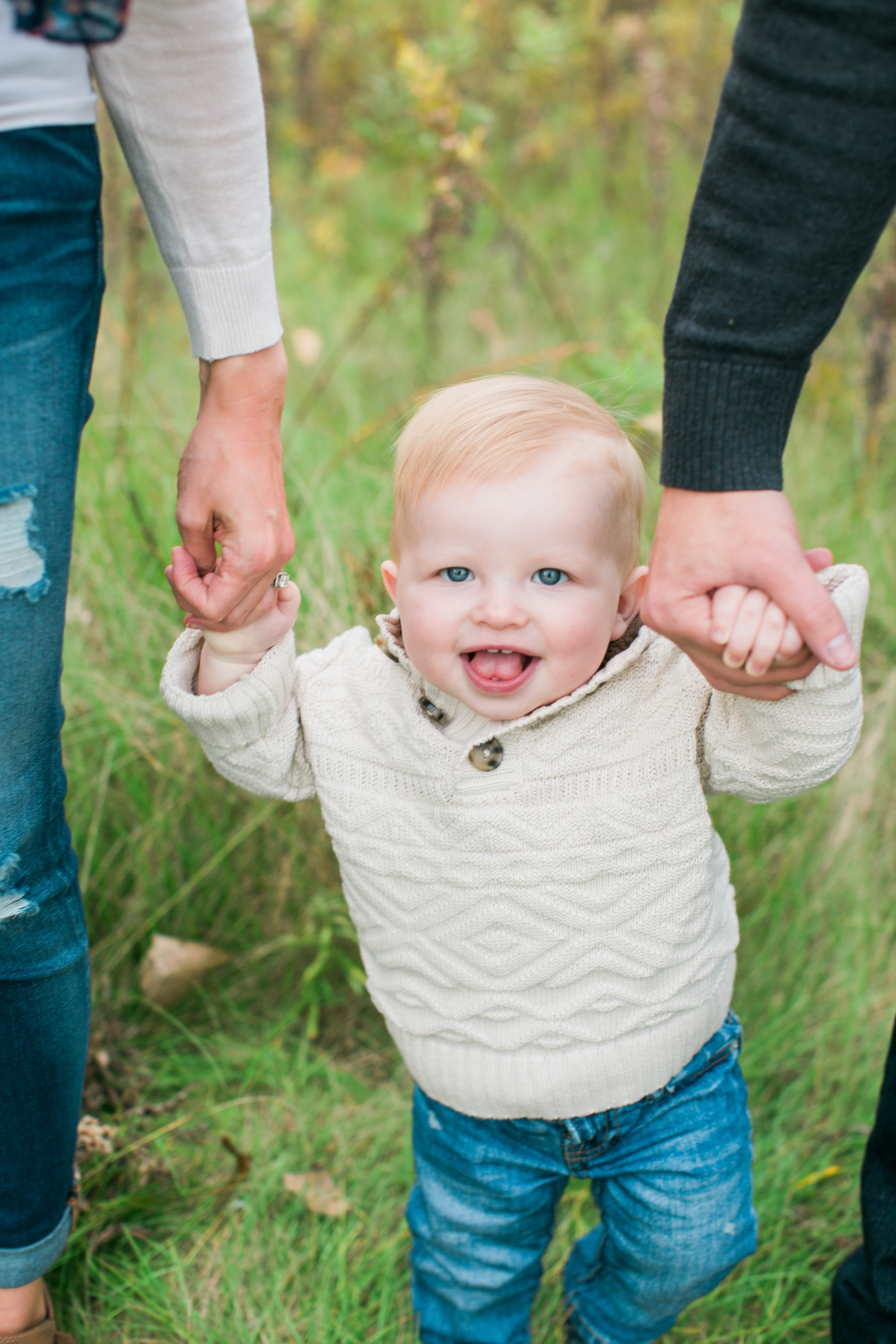 Toddler one year old holding mom and dads hands in rustic field in Minnesota fall family session Minnesota family photographer Mallory Kiesow Photography