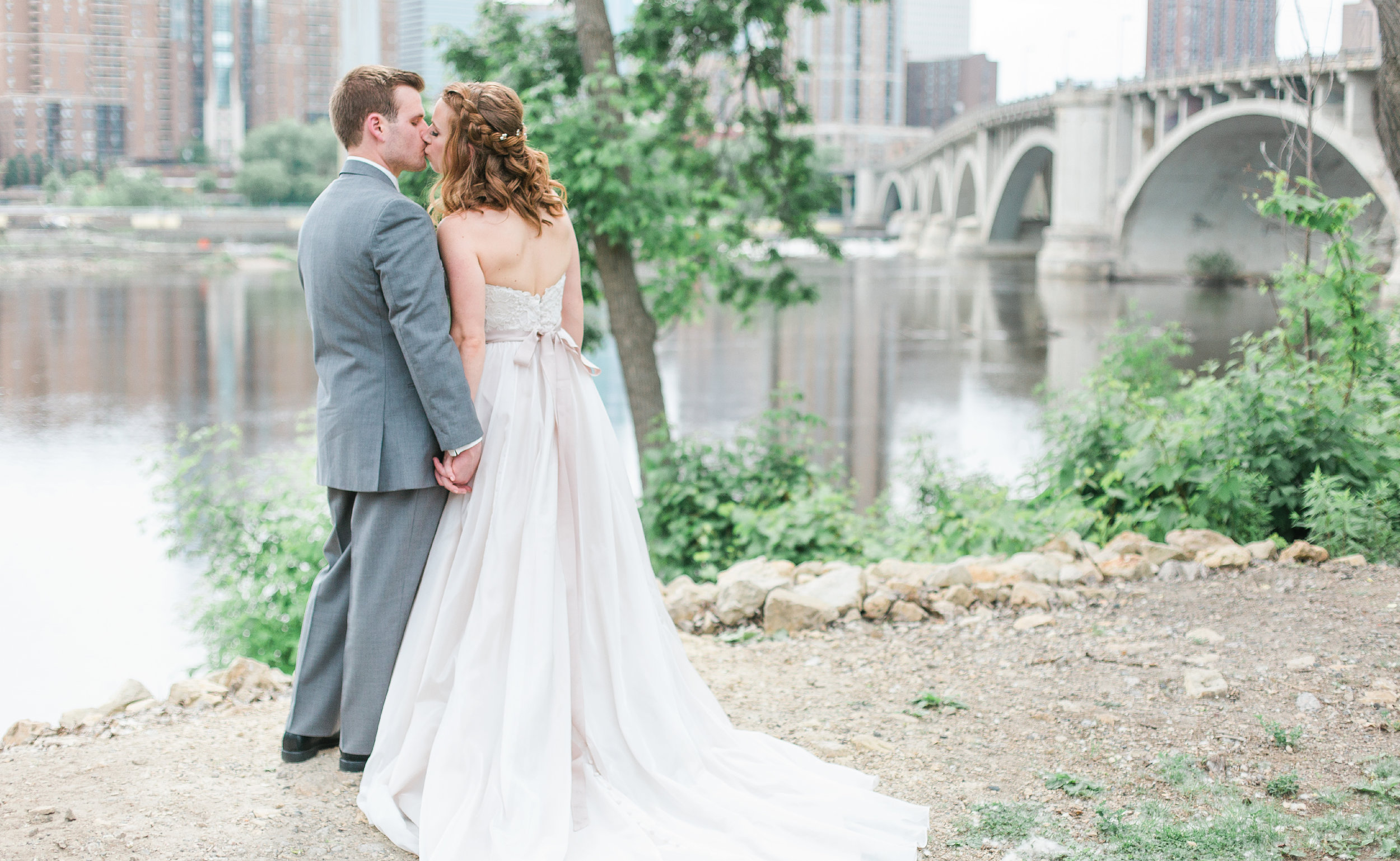 Bride and groom kissing in front of stone arch bridge in Minneapolis St Anthony Main Minneapolis Event Center wedding Minnesota wedding photography Mallory Kiesow photography