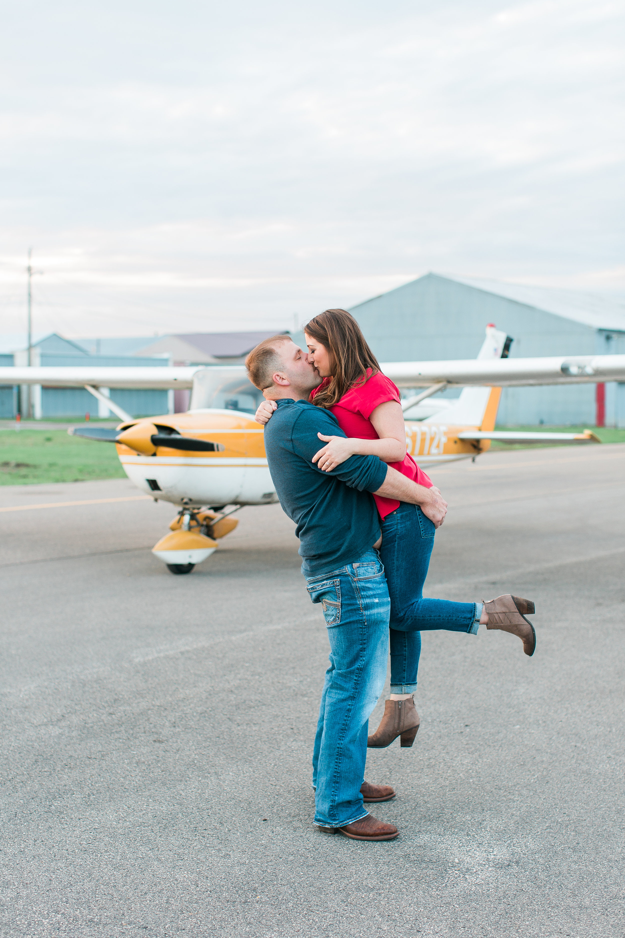 Engaged couple kissing and guy holding girl in front of airplane at Flying Cloud Airport in Eden Prairie for engagement session Minnesota engagement photographer Mallory Kiesow Photography