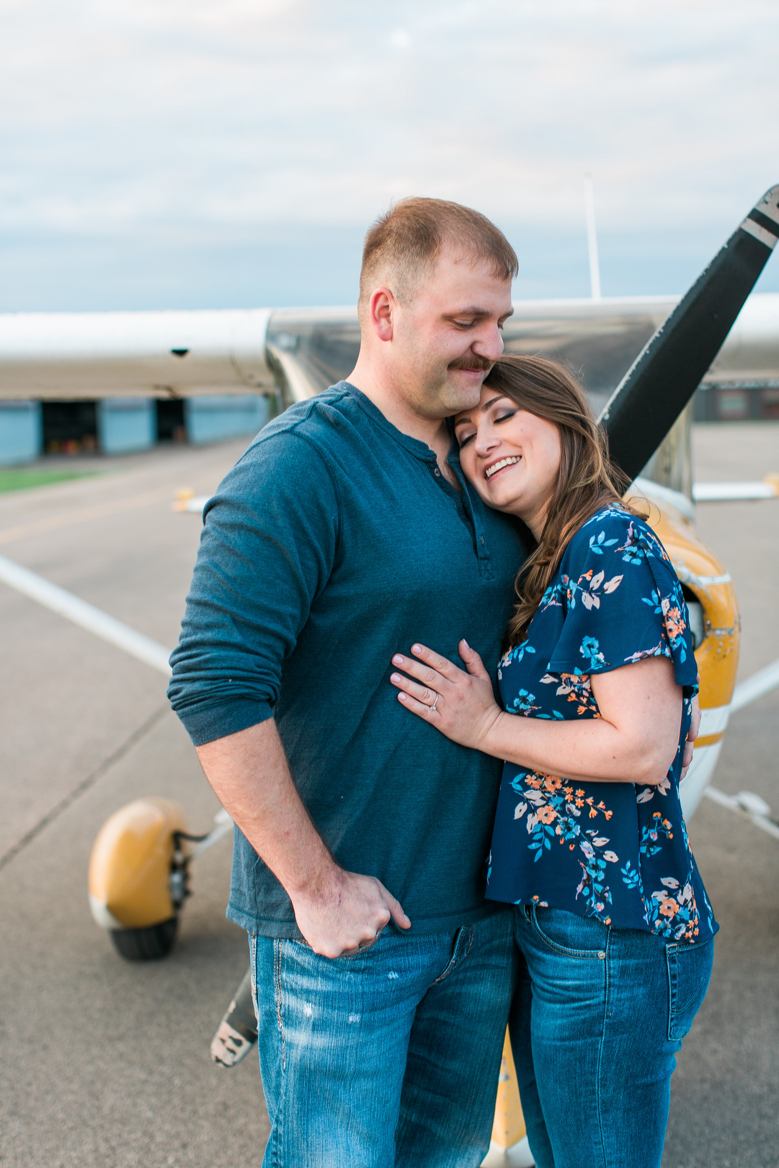 Engaged couple embracing in front of airplane at Flying Cloud Airport in Eden Prairie Minnesota Minnesota engagement photographer Mallory Kiesow Photography