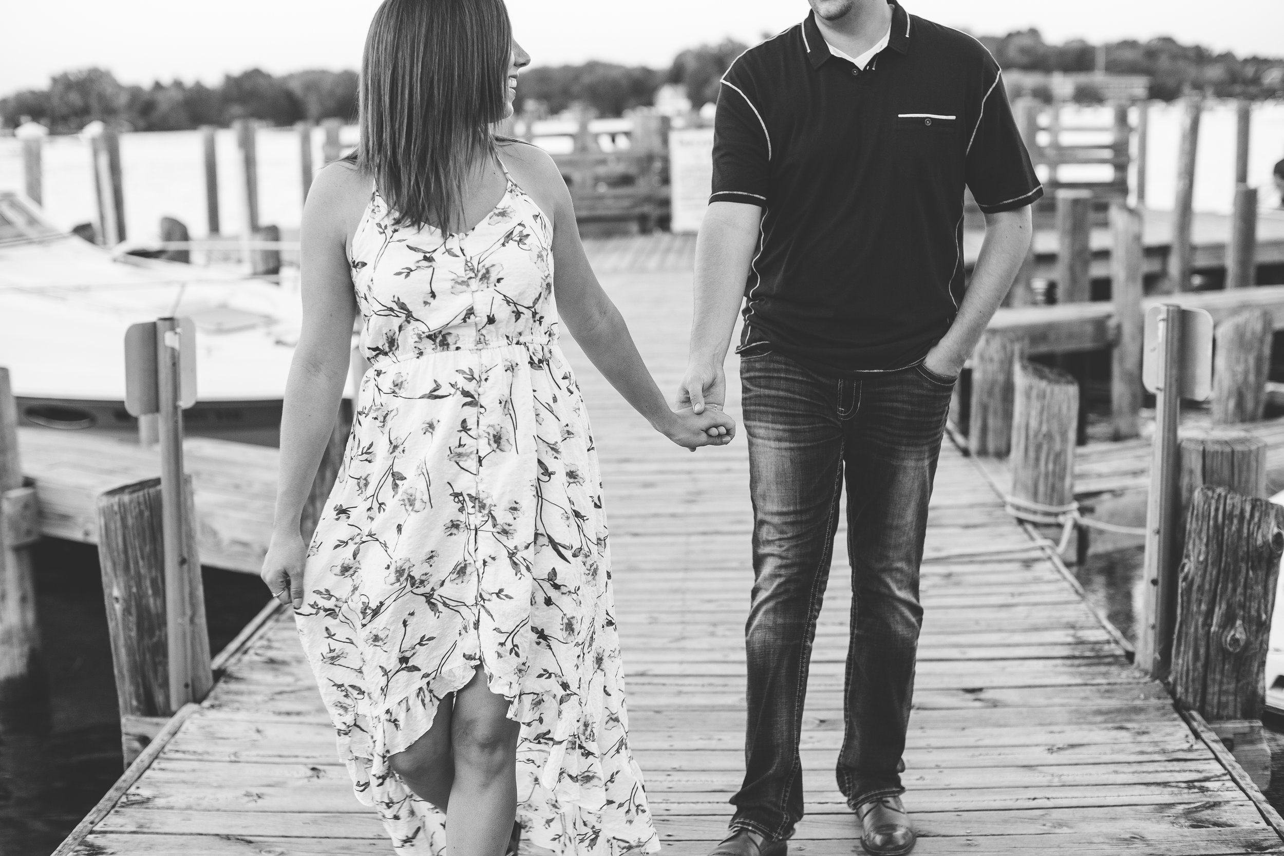 Engaged couple walking and holding hands in black and white photo on Lake Minnetonka dock in Excelsior Minnesota engagement session Minnesota engagement photographer Mallory Kiesow Photography