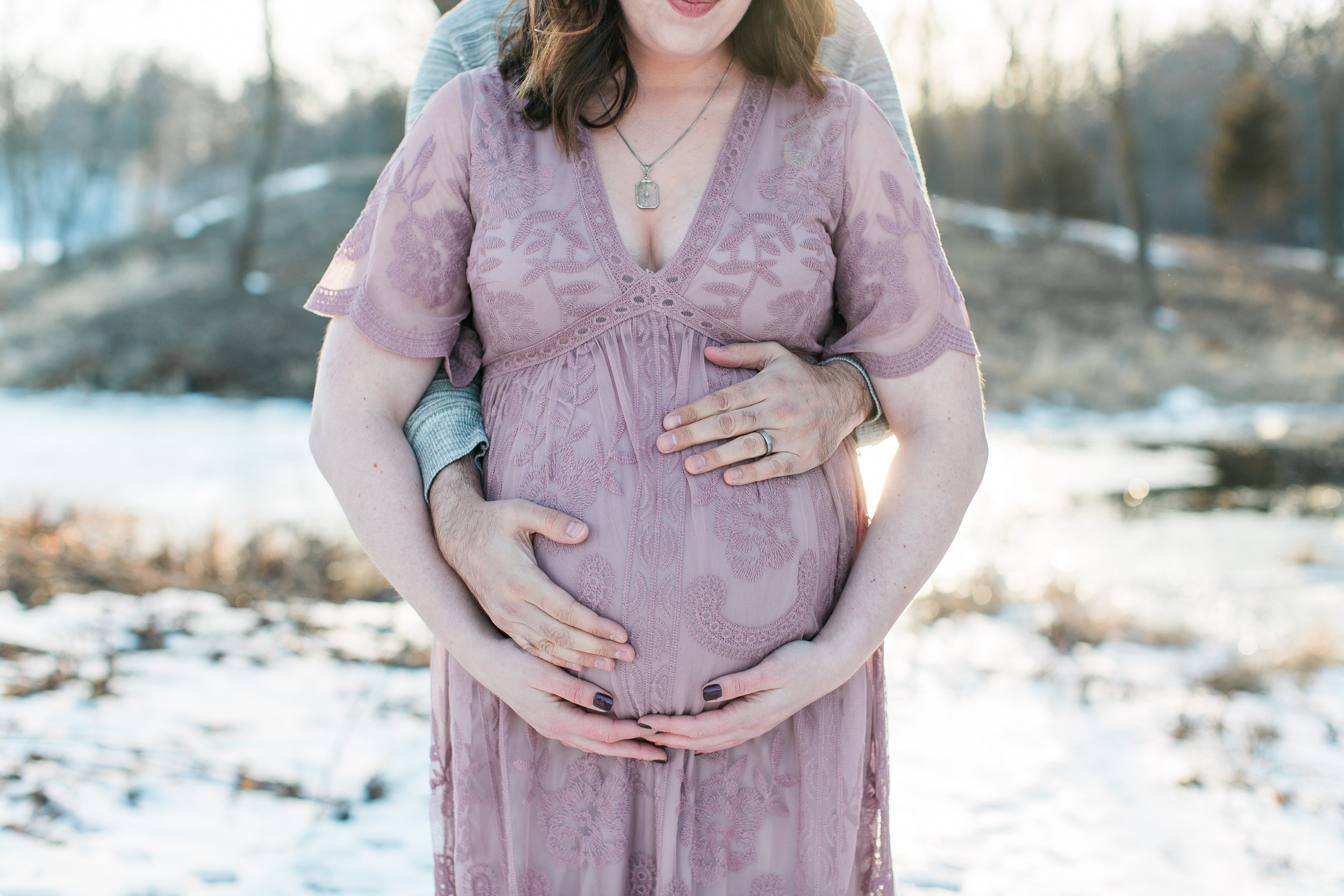 Expecting mother holding pregnant belly in pink lace dress in winter maternity photos Minnesota maternity photographer Mallory Kiesow Photography