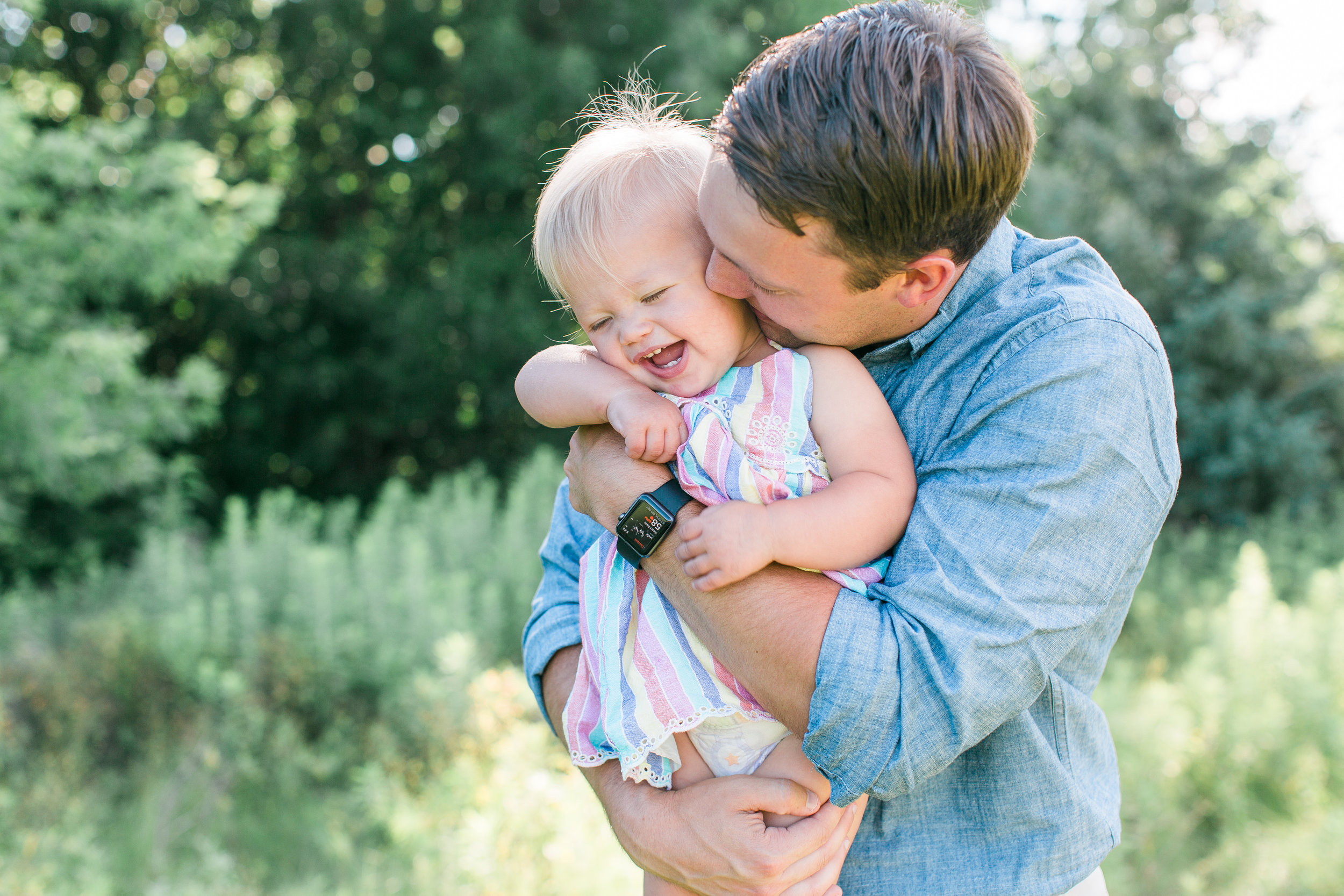 Dad cuddling and making baby laugh in rural field in Minnesota for family photos Minnesota family photographer Mallory Kiesow Photography