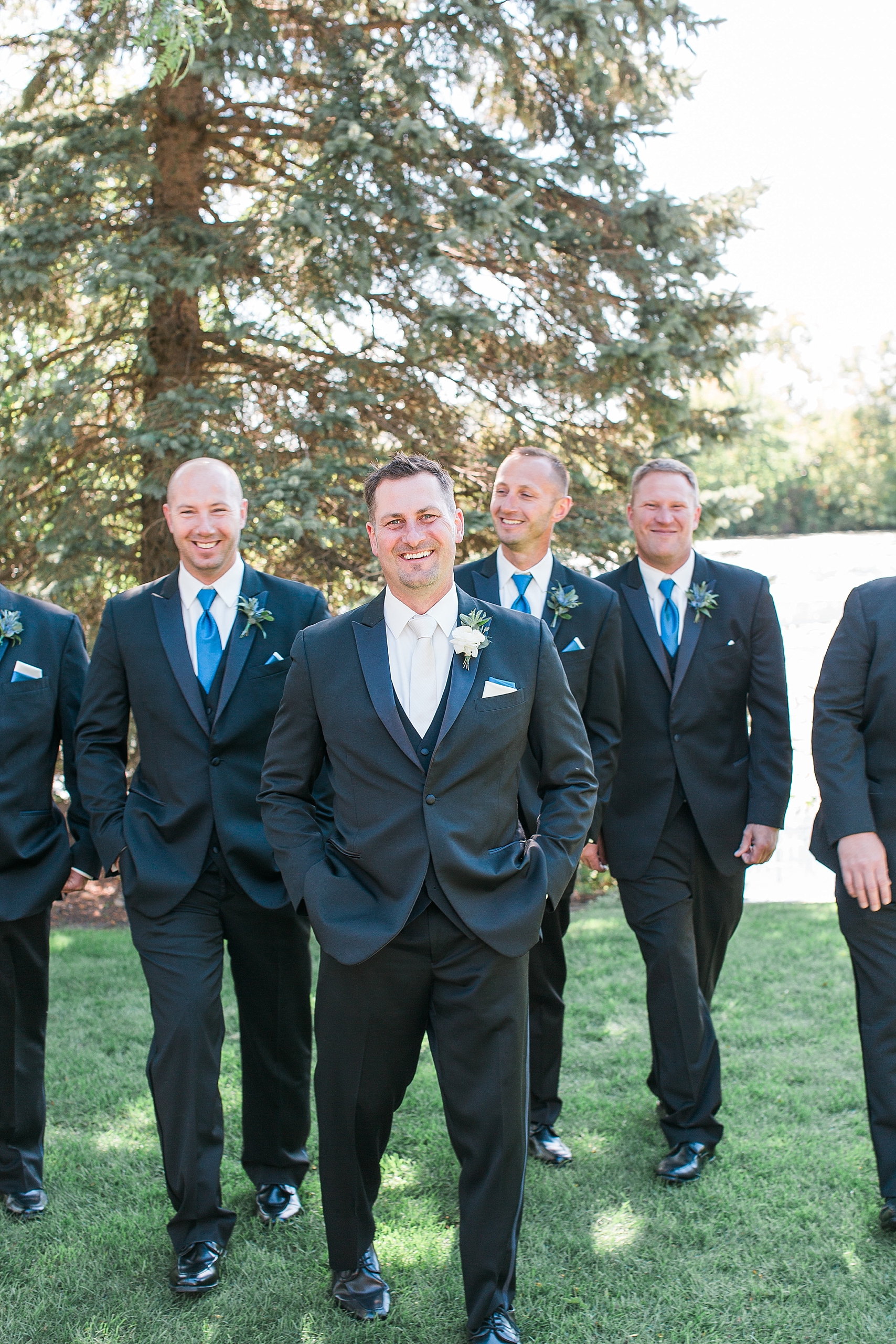 Groom and groomsmen in black suits suits walking and laughing on wedding day at the Chart House Summer Wedding Lakeville Minnesota Minneapolis Wedding Photographer Mallory Kiesow