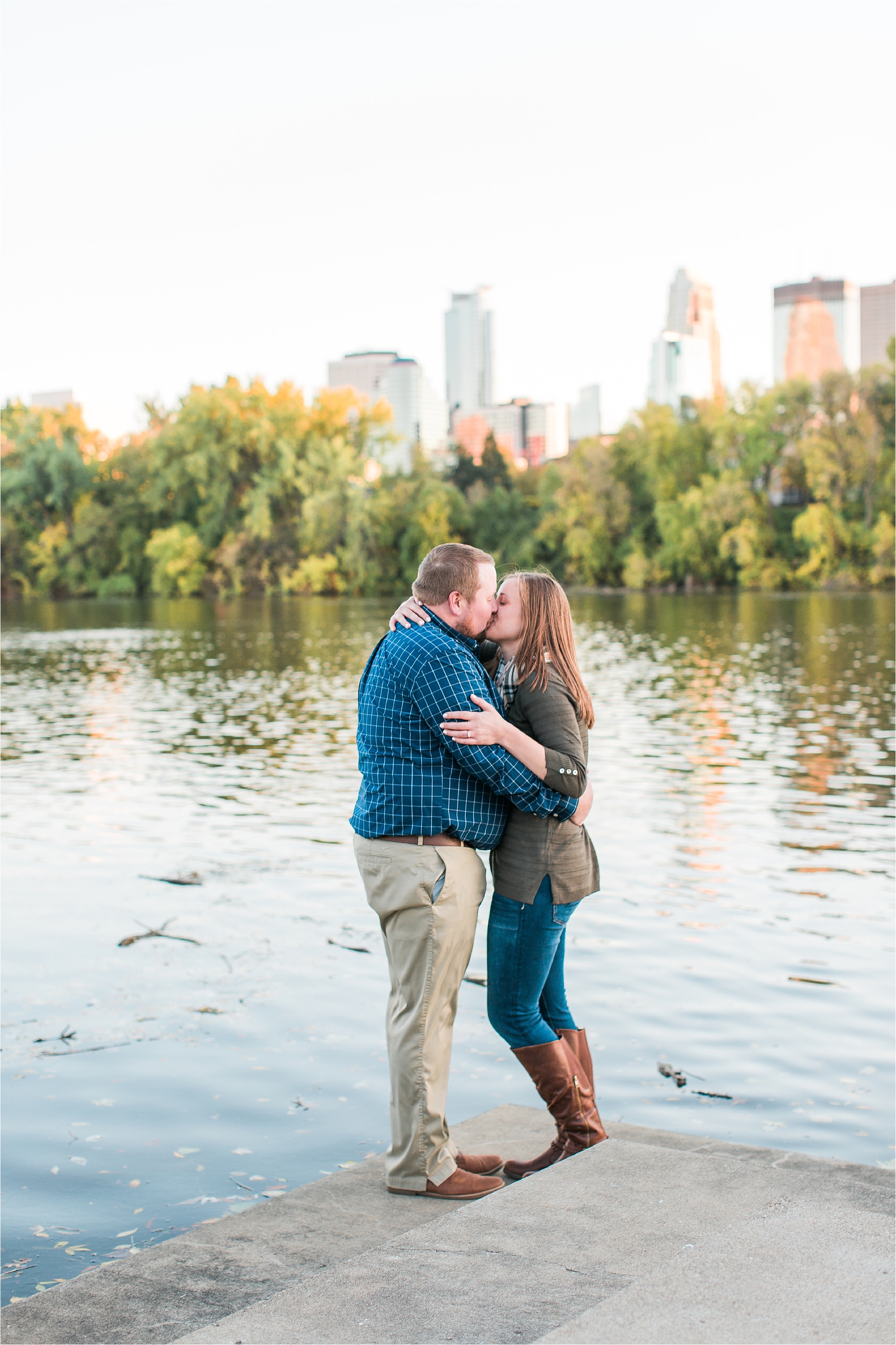 Engaged couple embracing in front of water with Minneapolis city skyline in the background at Boom Island Park in Minneapolis Mallory Kiesow Photography