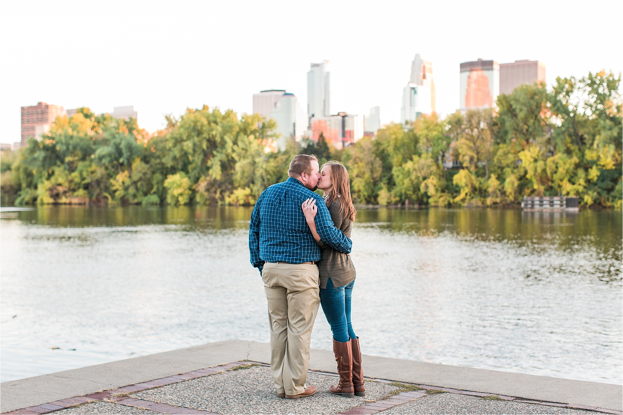 Engaged couple kissing with Minneapolis city skyline in the background at Boom Island Park in Minneapolis Mallory Kiesow Photography