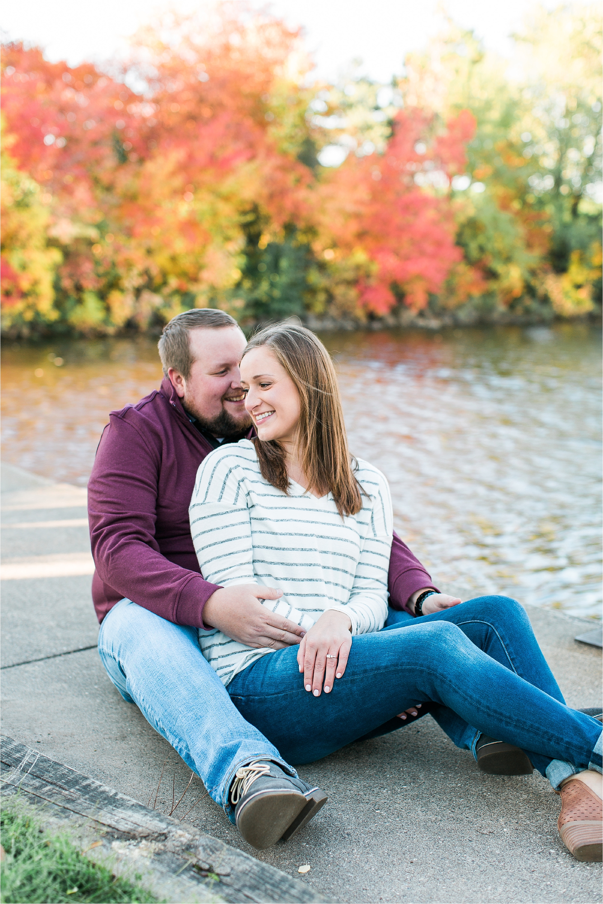 Engaged couple sitting along riverside in Minneapolis fall engagement session at Boom Island Park in Minneapolis