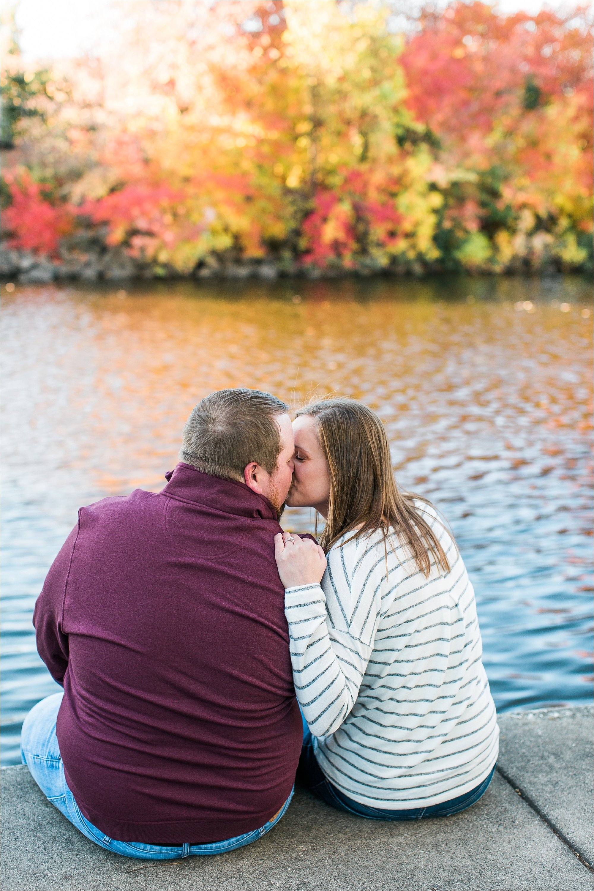 Engaged couple sitting along riverside in Minneapolis fall engagement session at Boom Island Park in Minneapolis