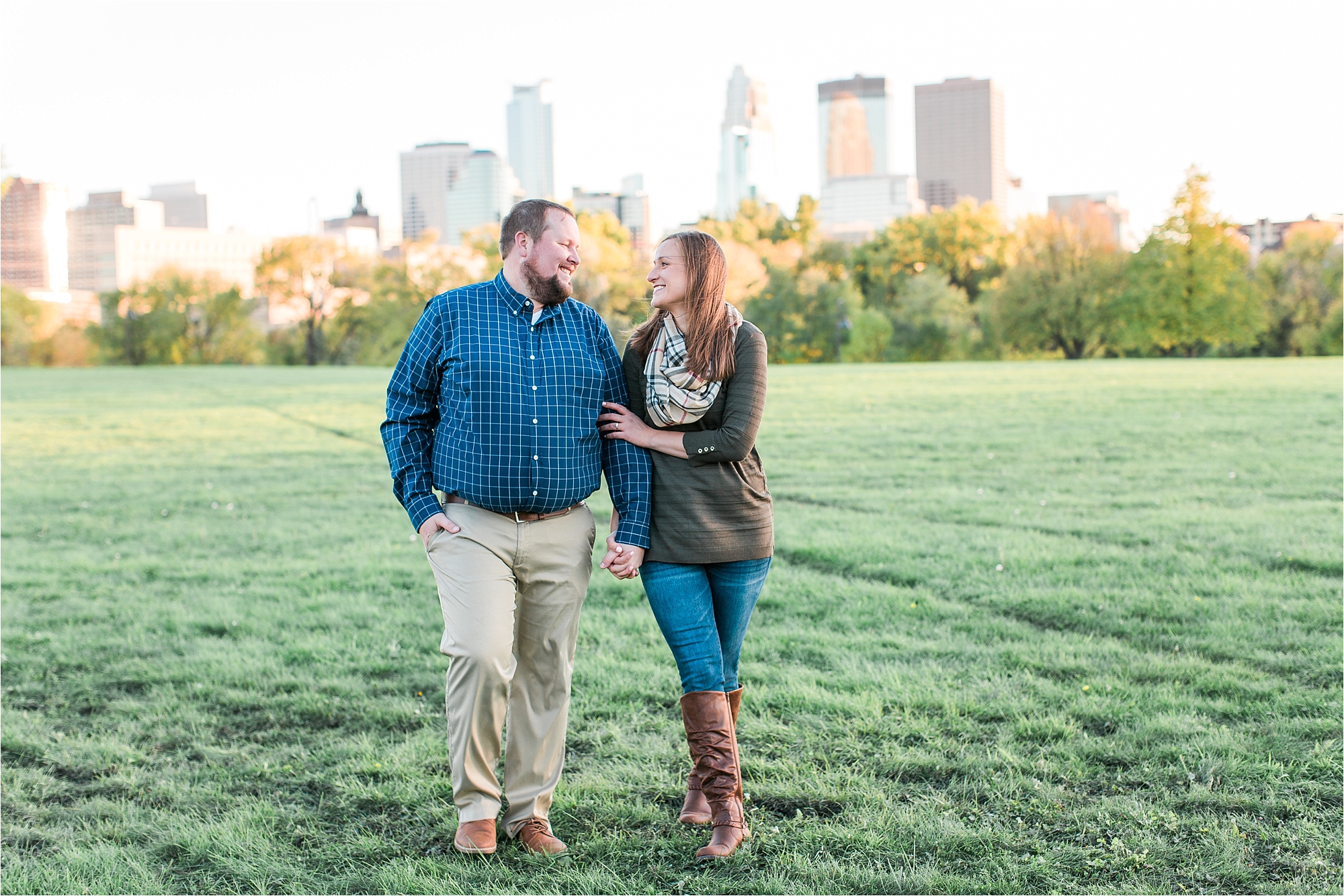 Engaged couple walking with Minneapolis city skyline in the background at Boom Island Park in Minneapolis Mallory Kiesow Photography