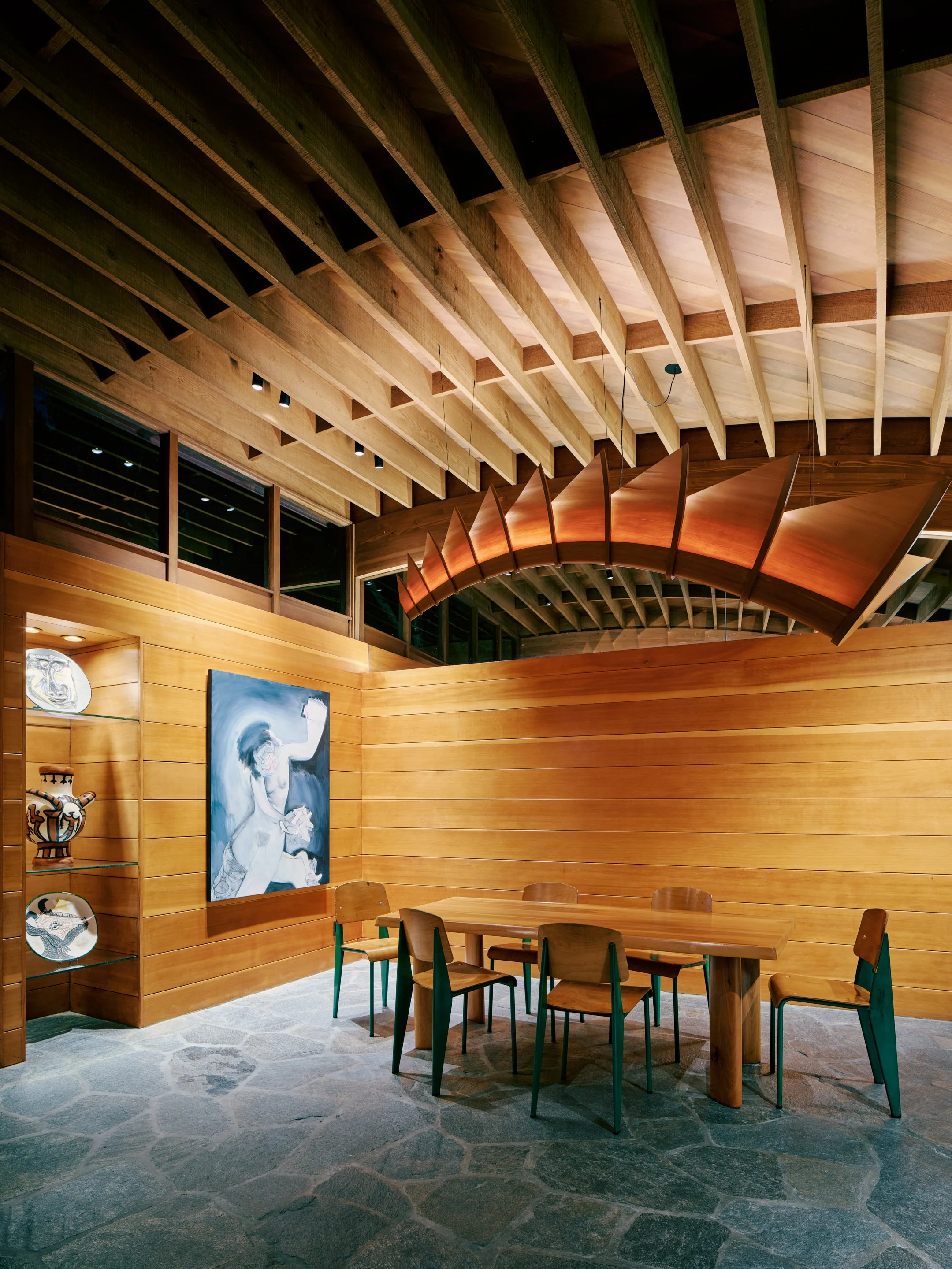 Evening interior view of The Dragon custom wood chandelier lit above the dining table at Lautner's Castle, highlighting Douglas fir ceiling beams and Bouquet Canyon stone floor.