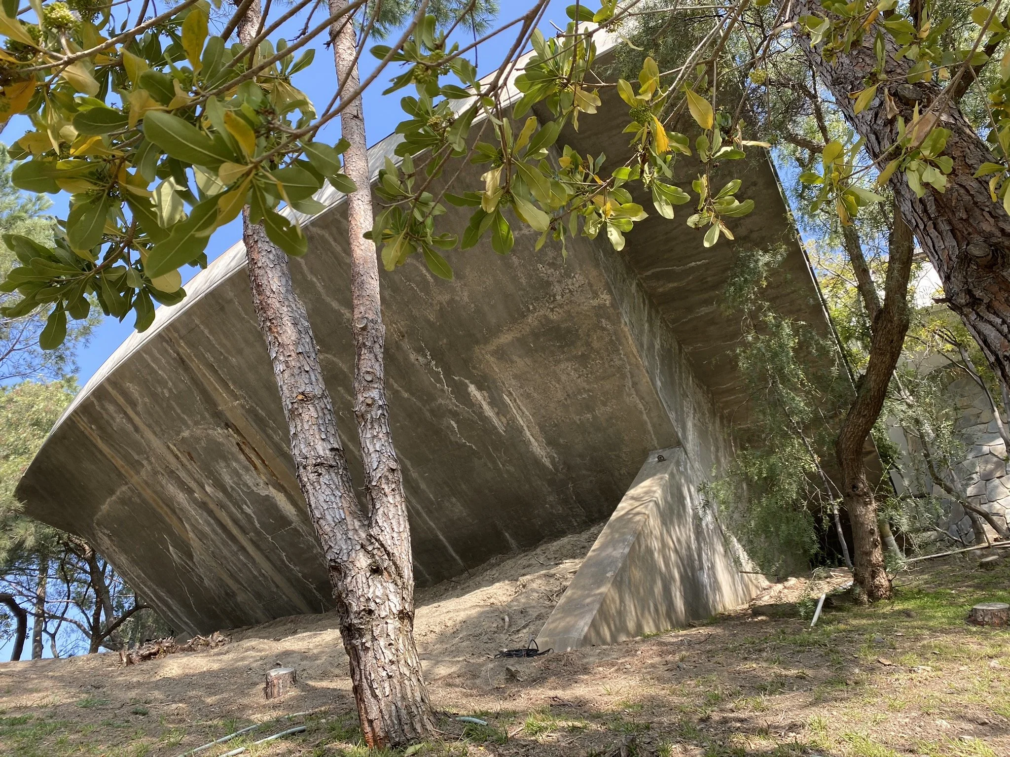 Low angle exterior view of the original 1982 concrete cantilevered pool at Lautner’s Castle, showing the structural void and hillside before renovation by Conner + Perry Architects.