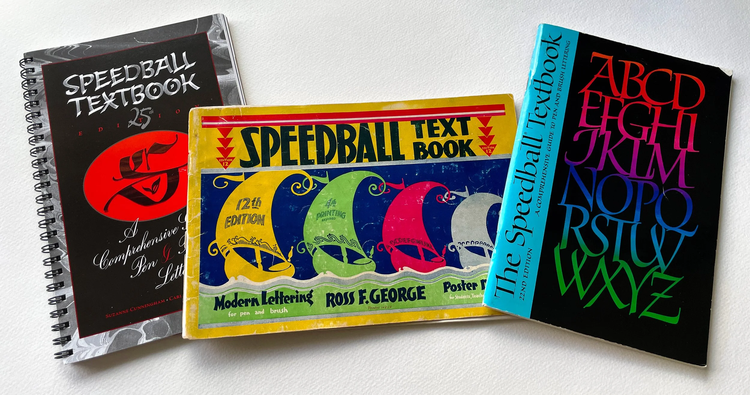 Three editions of the Speedball Textbook—the 12th, 22nd, and 25th editions—are laid out next to each other